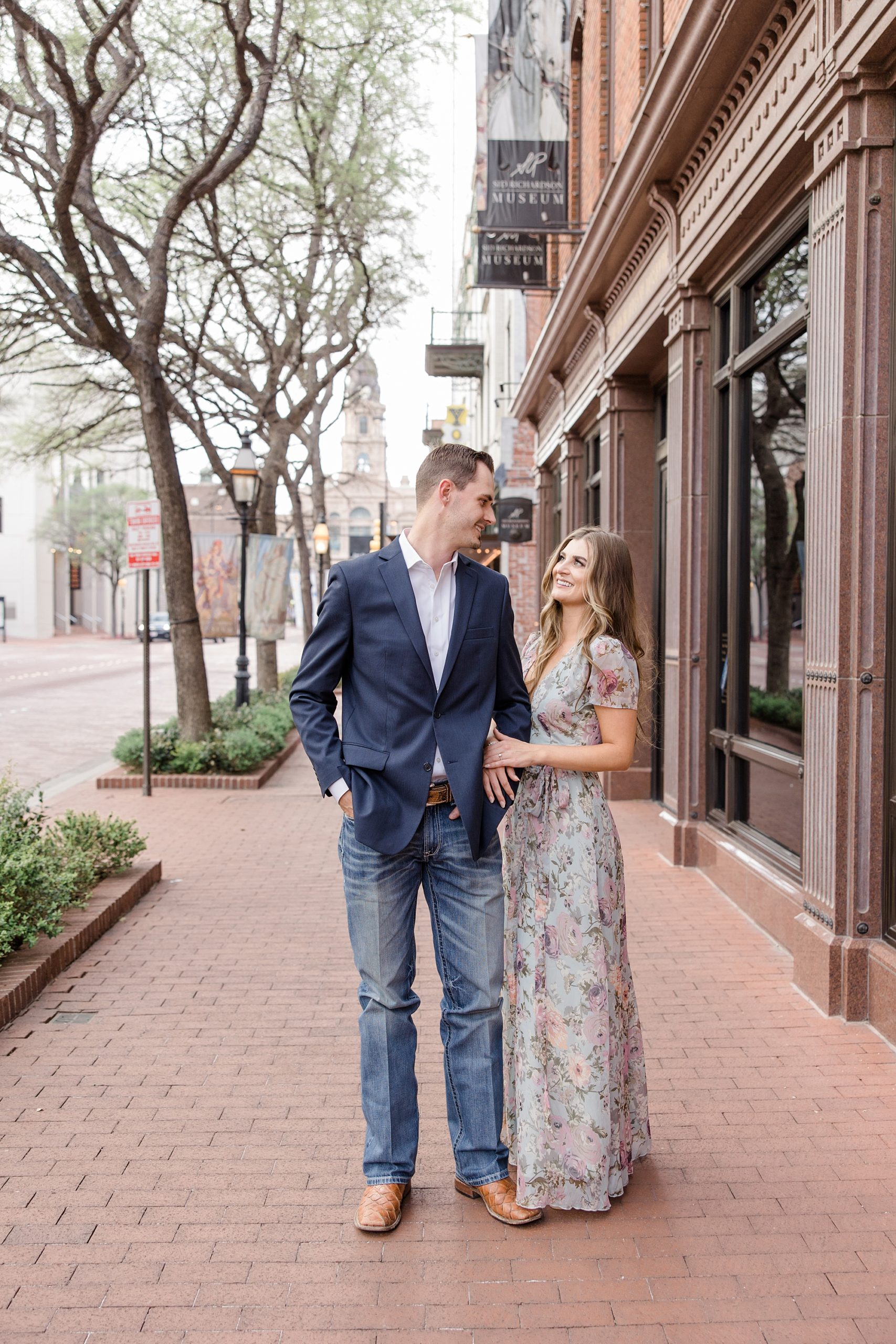 engaged couple stands on sidewalk near Sundance Square