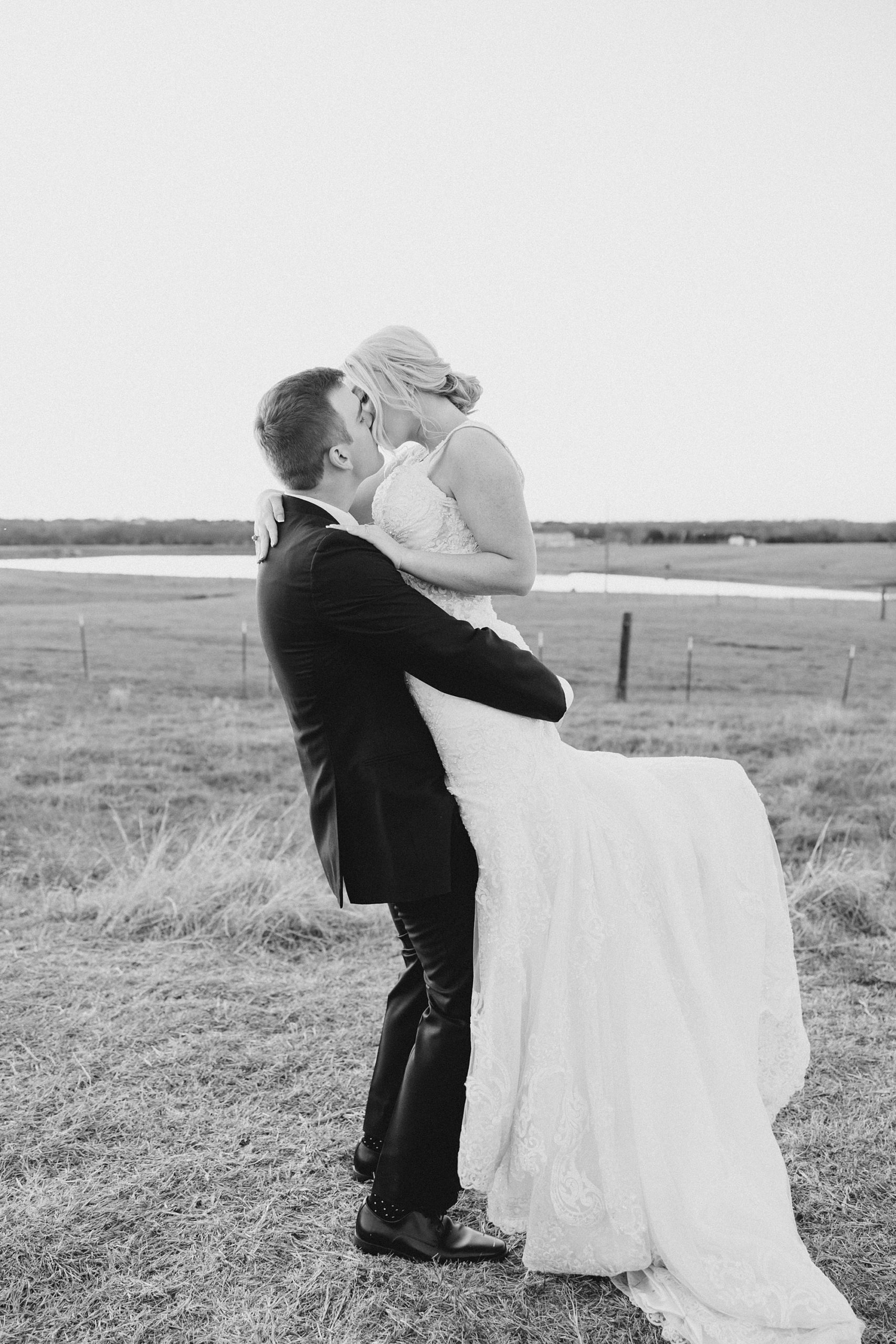 groom lifts bride in field during wedding portraits 