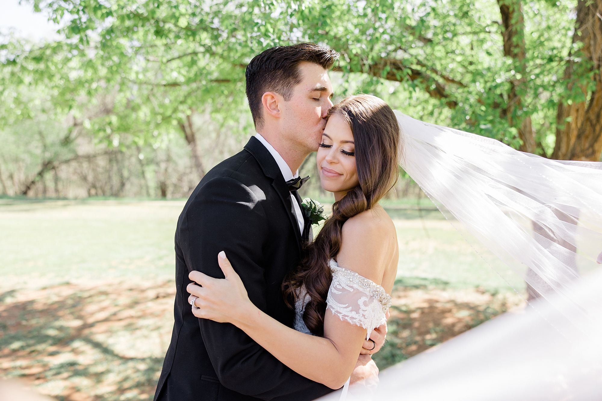 groom kisses bride's forehead with veil floating