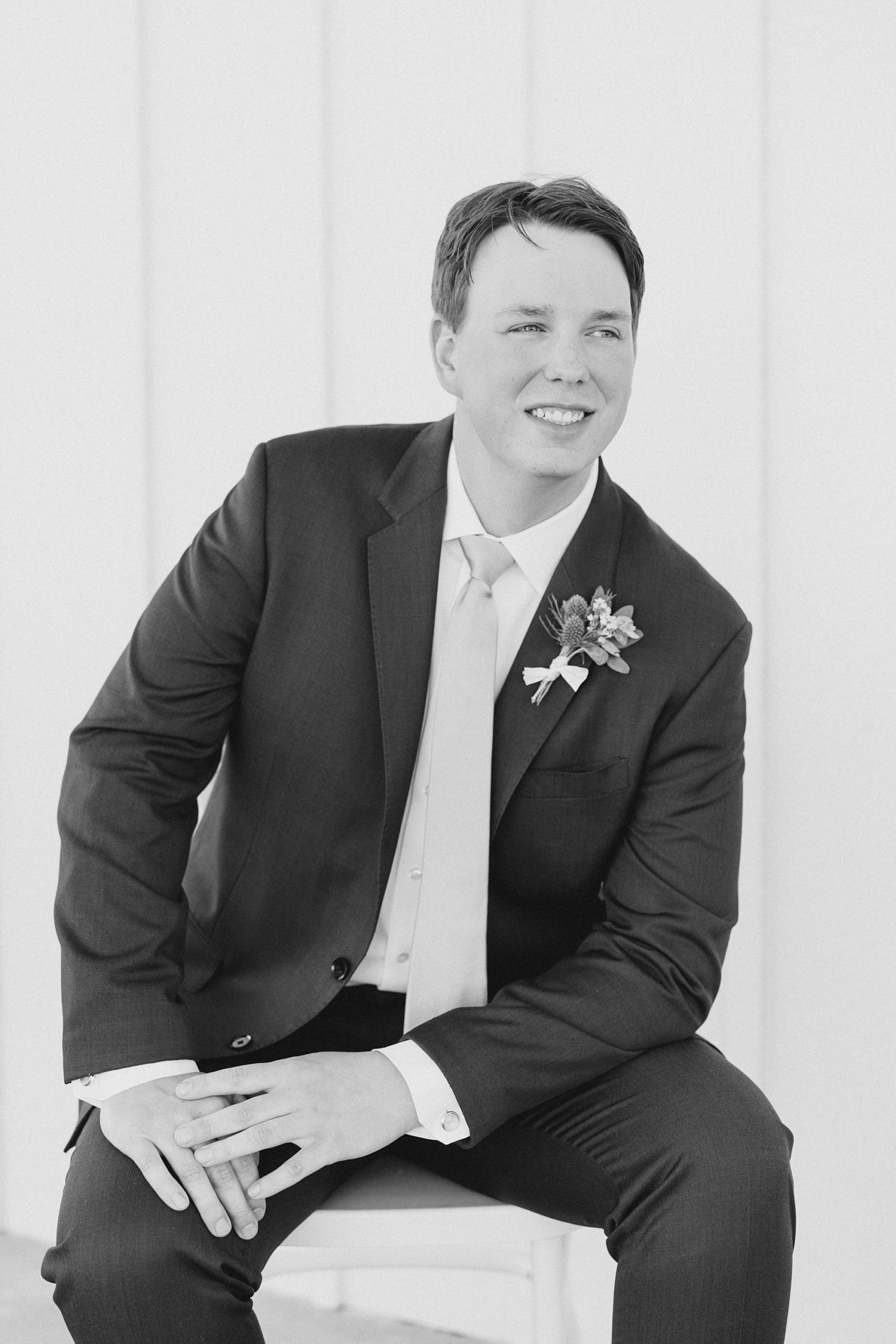 groom sits on stool leaning on leg in classic suit