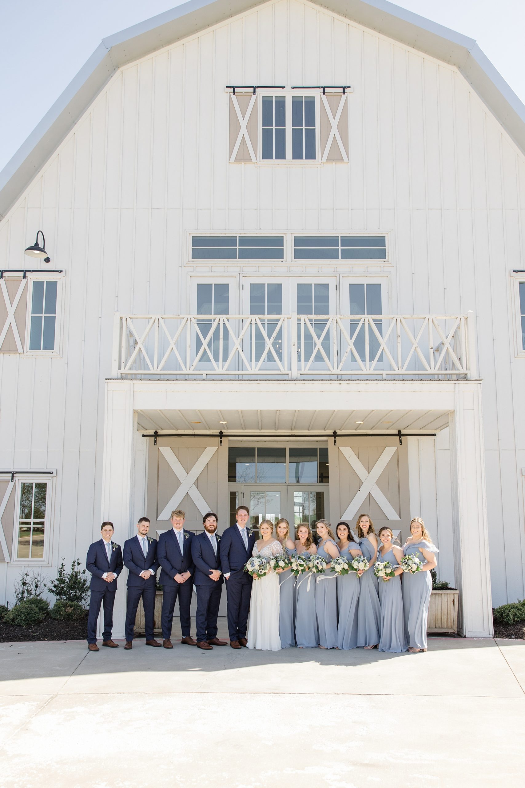 bride and groom stand with wedding party in navy suits and blue gowns