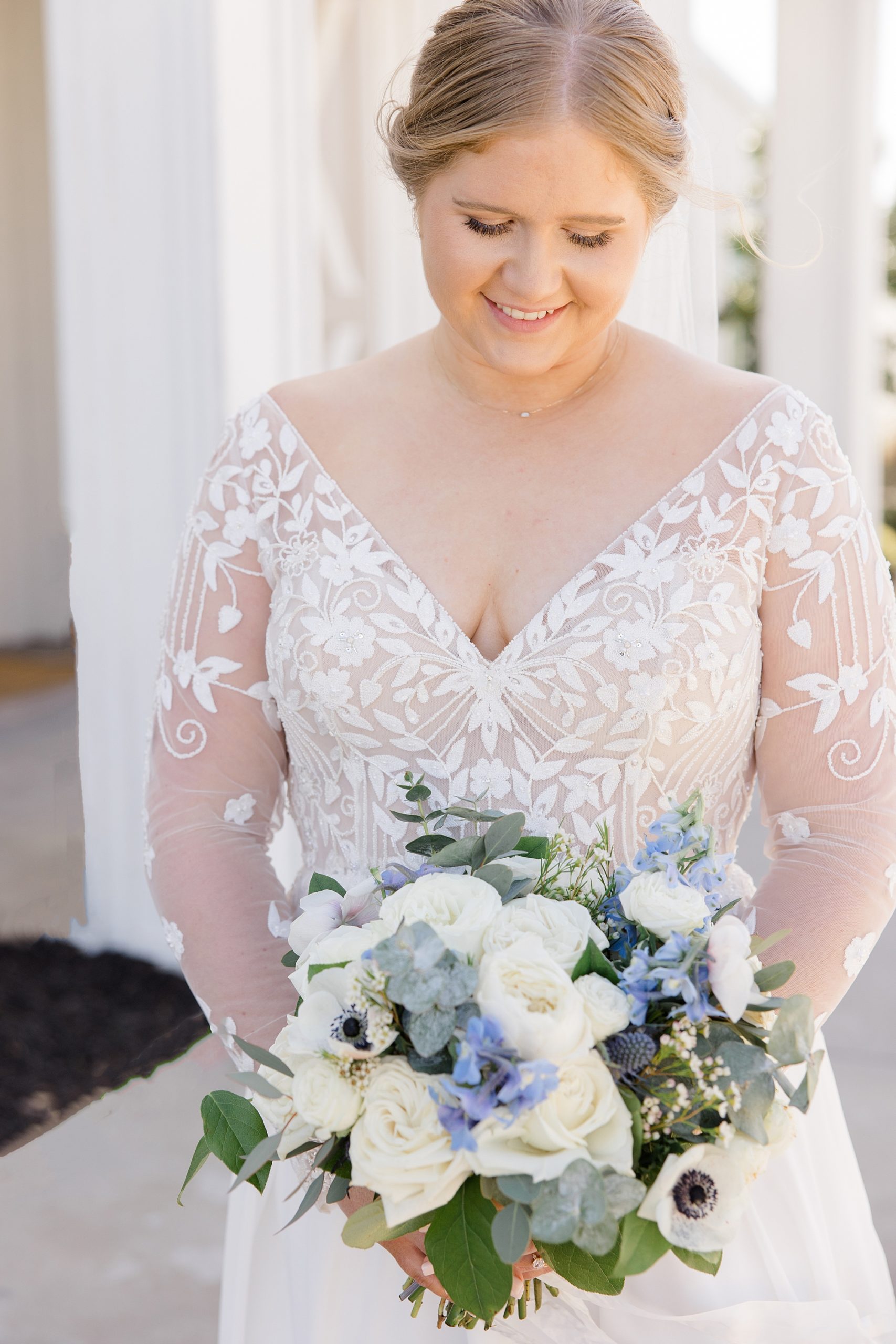 bride in wedding gown with lace sleeves looks down at spring bouquet