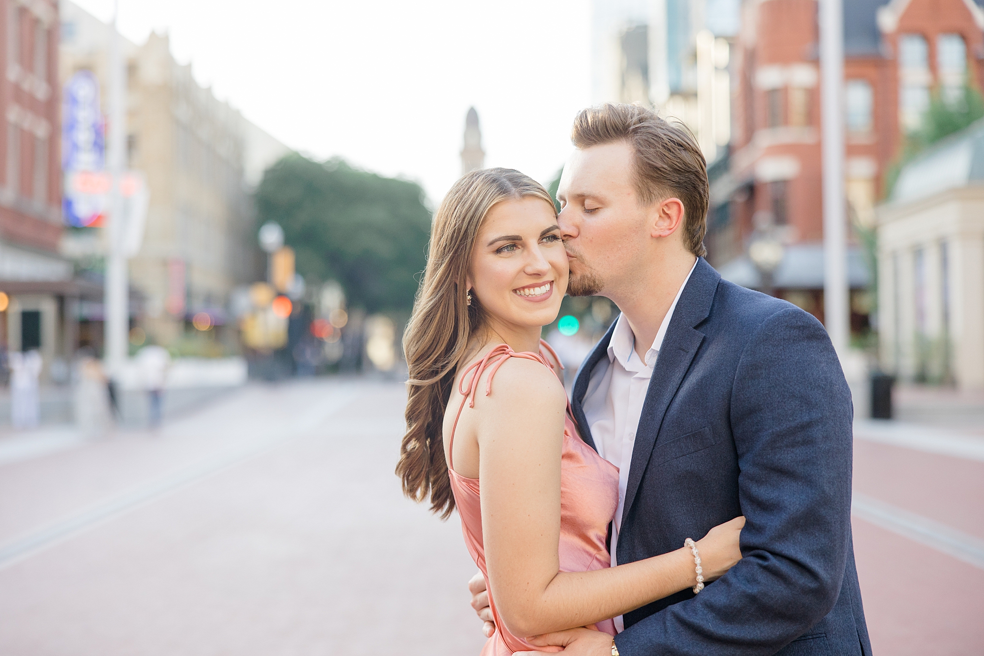 groom kisses fiancee's cheek during engagement photos in Sundance Square