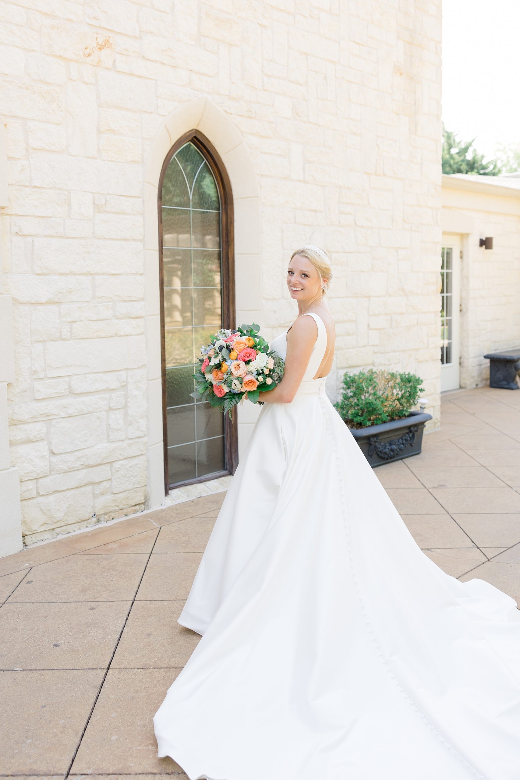 bride looks over shoulder holding bouquet with pink and orange flowers 