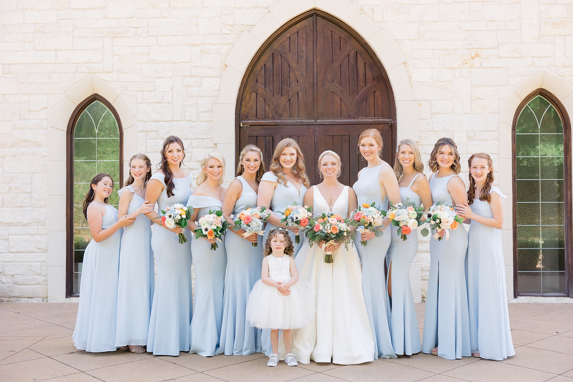 bride and bridesmaids in pale blue gowns pose by wooden door at Ashton Gardens