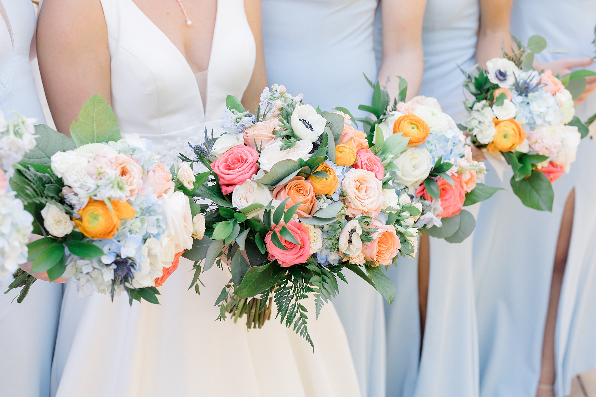 bride and bridesmaids hold pink and orange bouquets in blue gowns