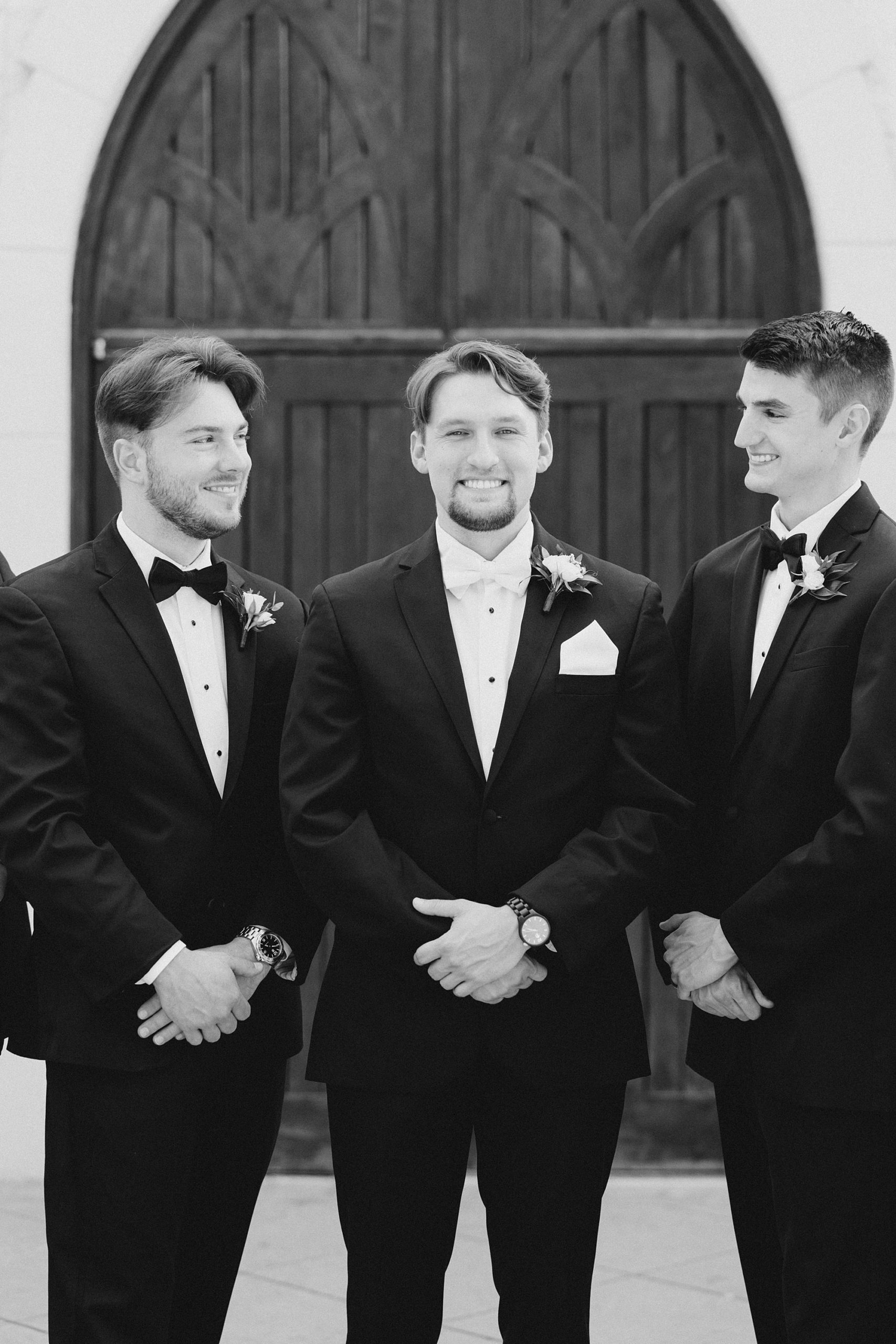 groom and groomsmen smile standing by wooden door