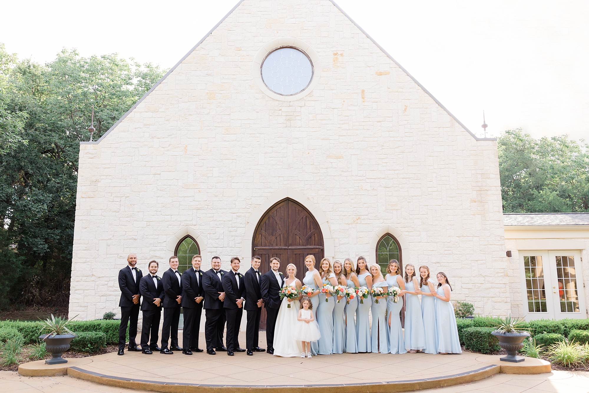 newlyweds stand with wedding party in tuxes and blue gowns