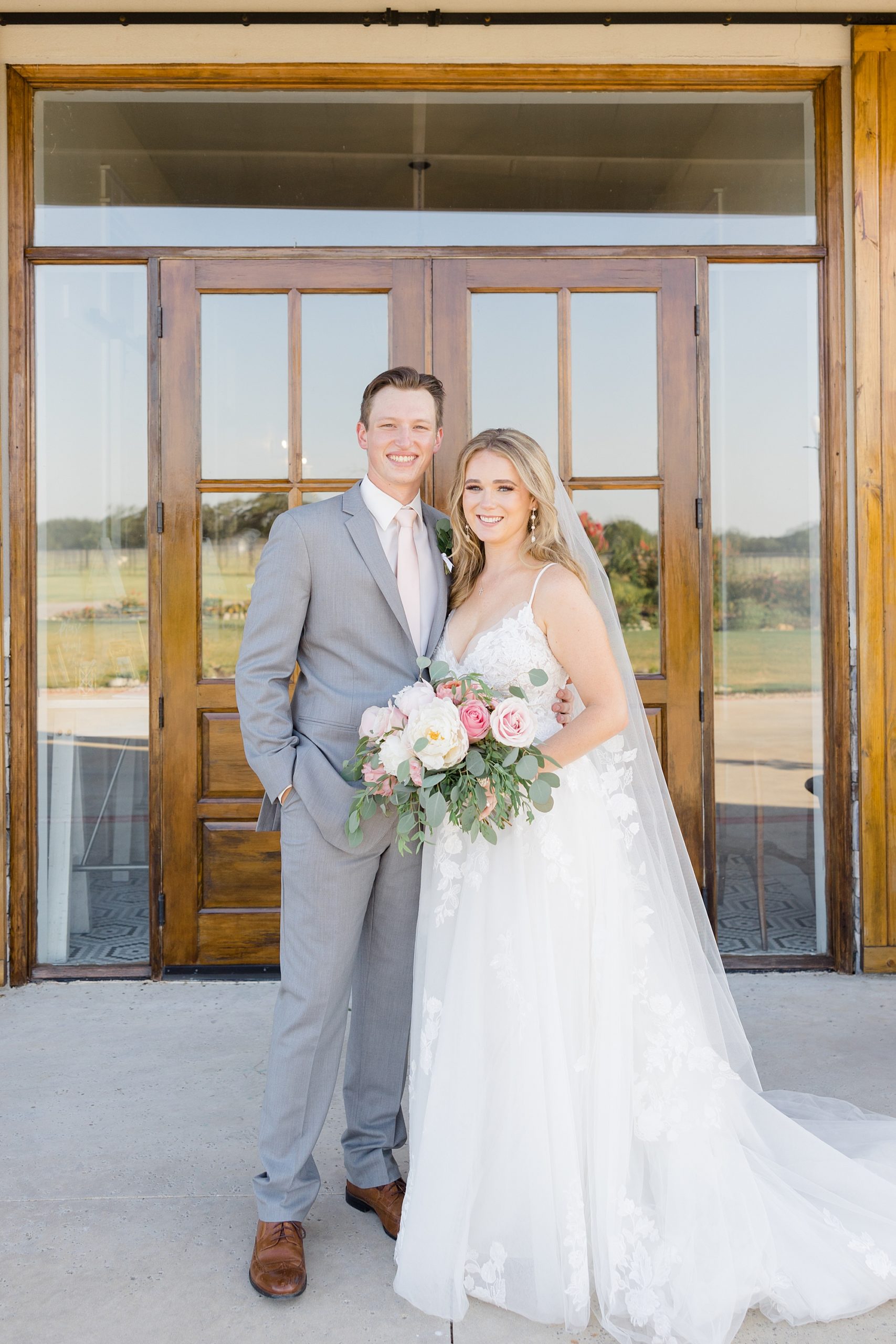 newlyweds pose outside wooden doors at Oak + Ivy