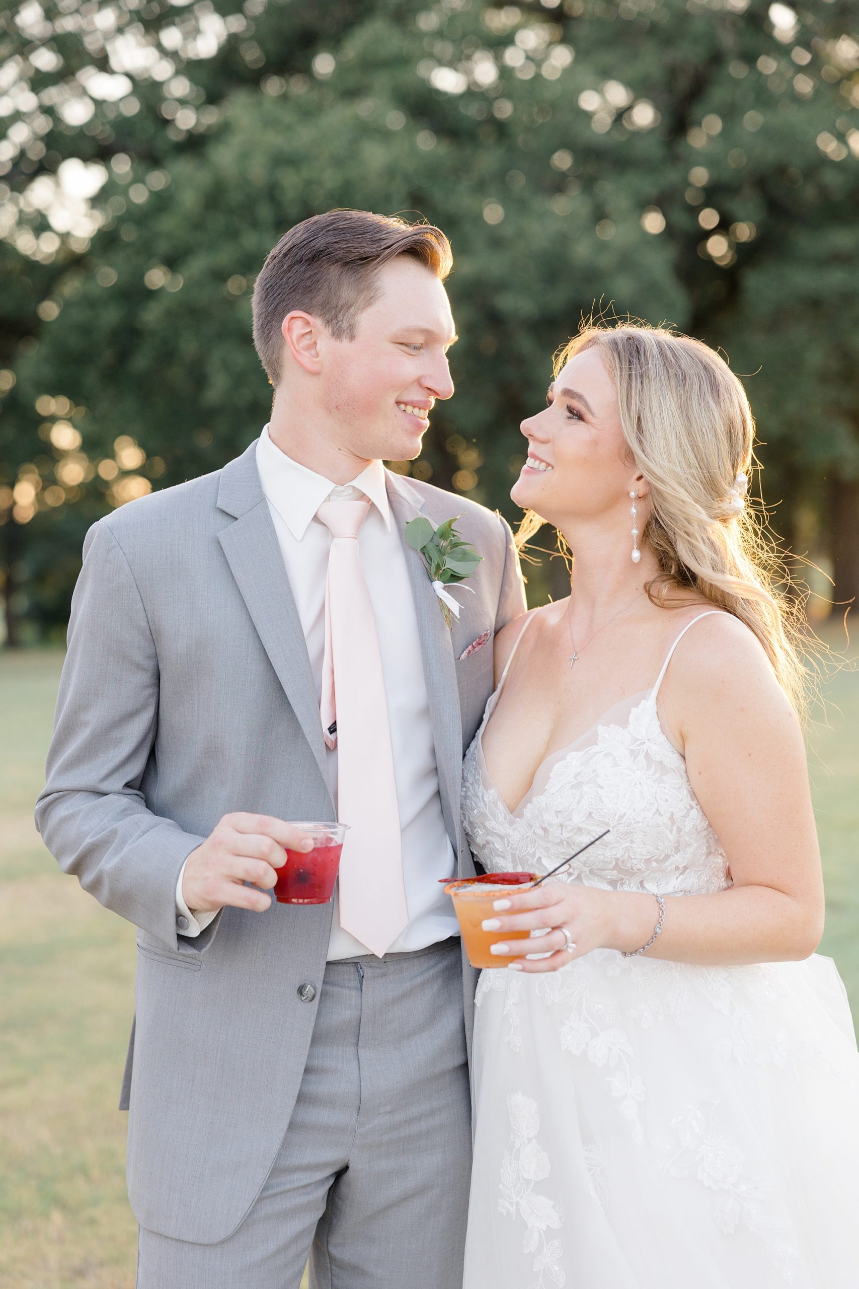 bride and groom hold signature cocktails smiling at each other 