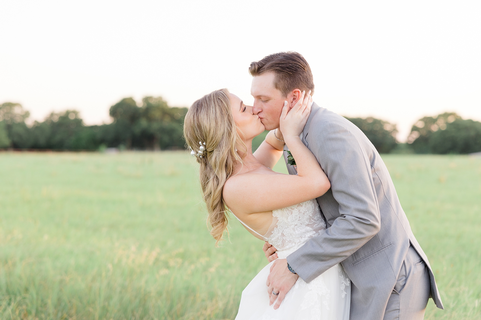 newlyweds kiss in field at sunset outside Oak + Ivy