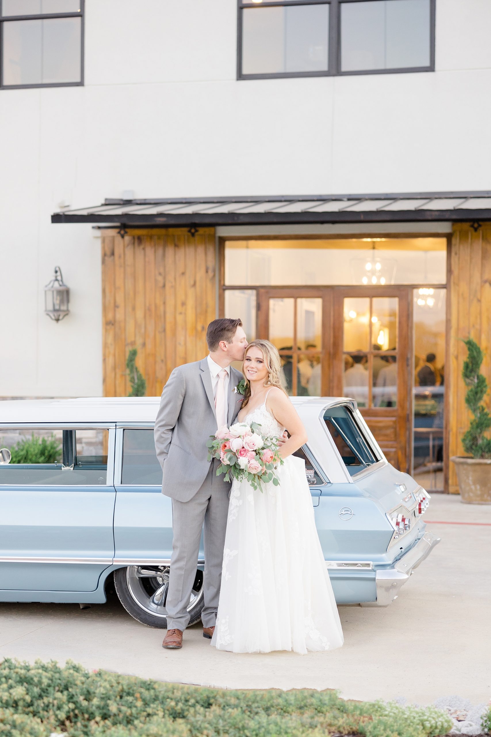 bride and groom pose by classic blue car outside Oak + Ivy