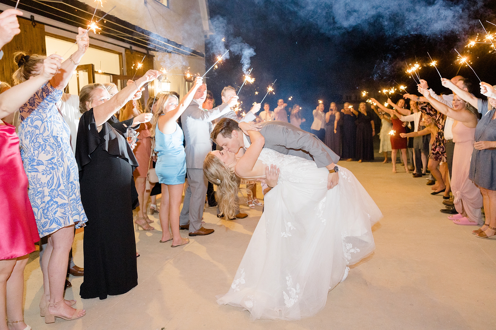 groom dips bride kissing her during sparkler exit from Oak + Ivy summer wedding