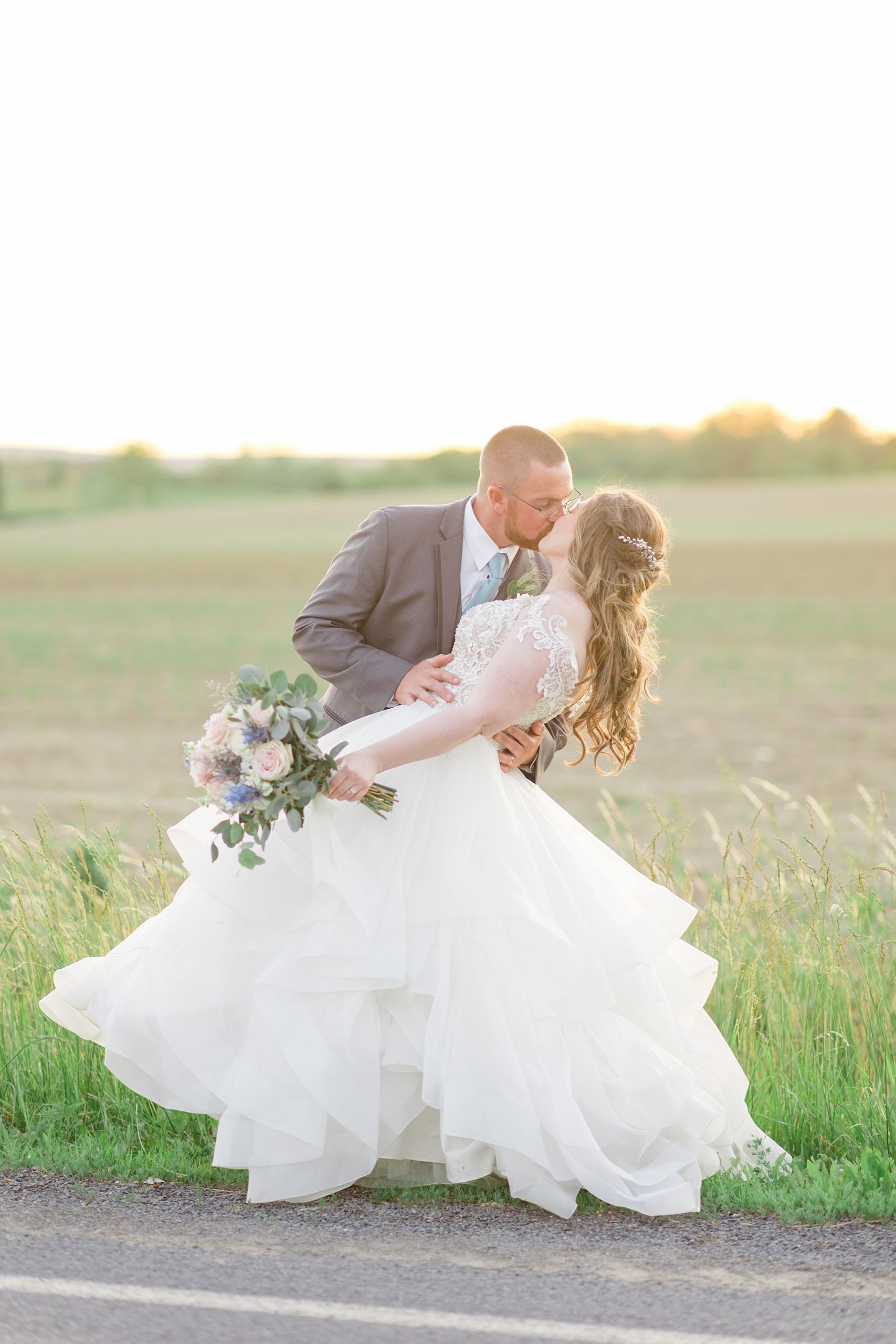 groom dips bride during portraits at sunset along field 