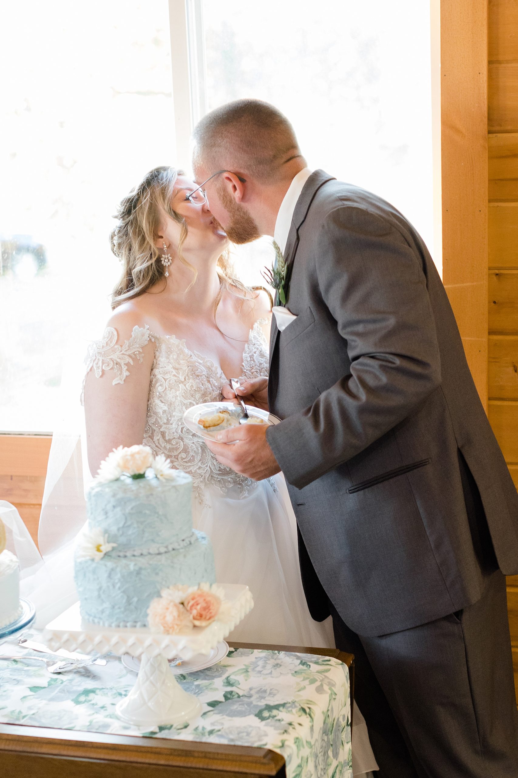 couple kisses by blue wedding cake at rustic New York wedding reception