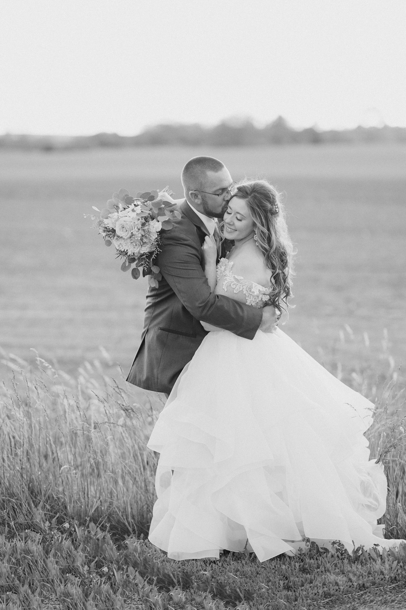 black and white portrait of newlyweds hugging in field