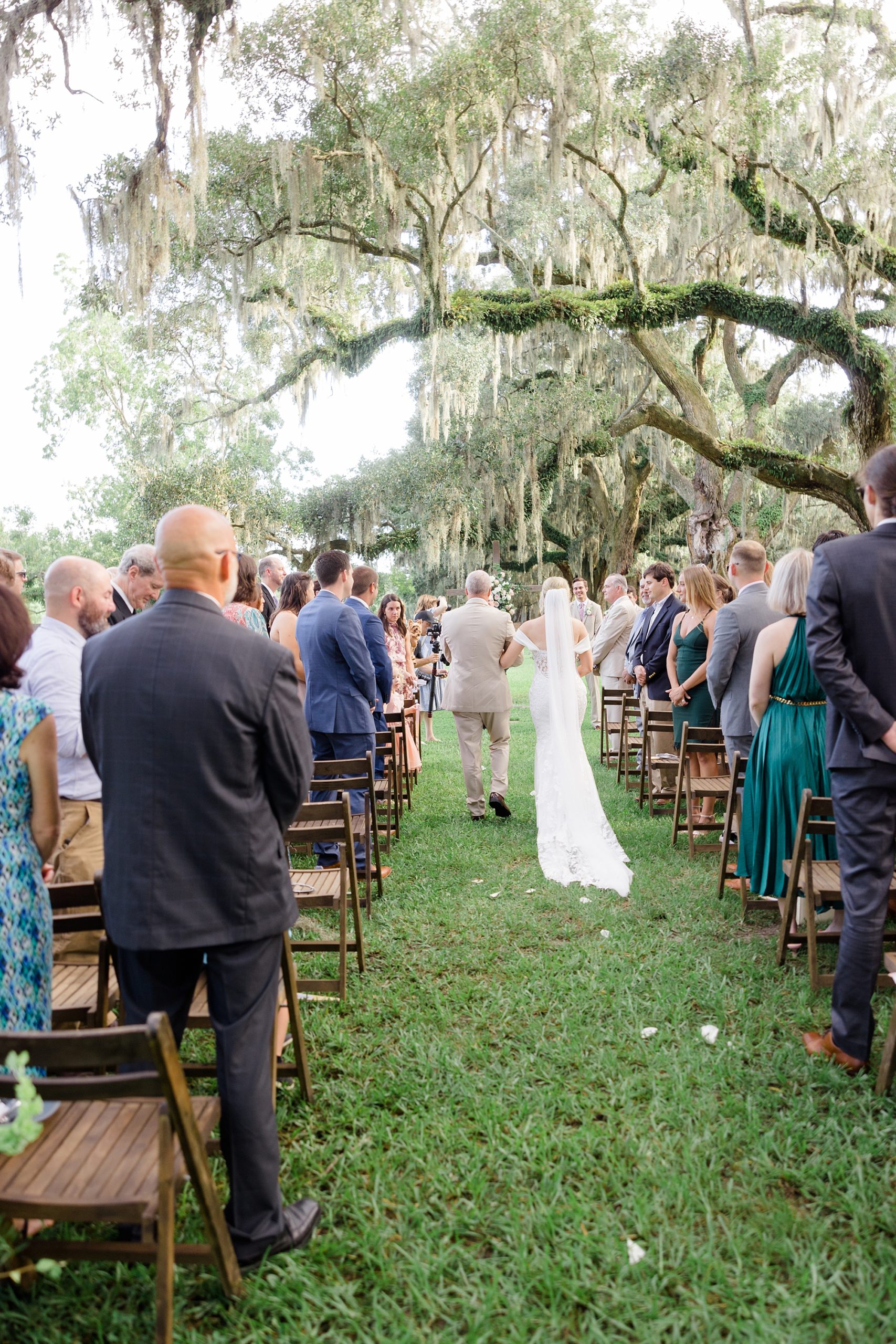 bride walks down aisle with father under oak trees at Boone Hall