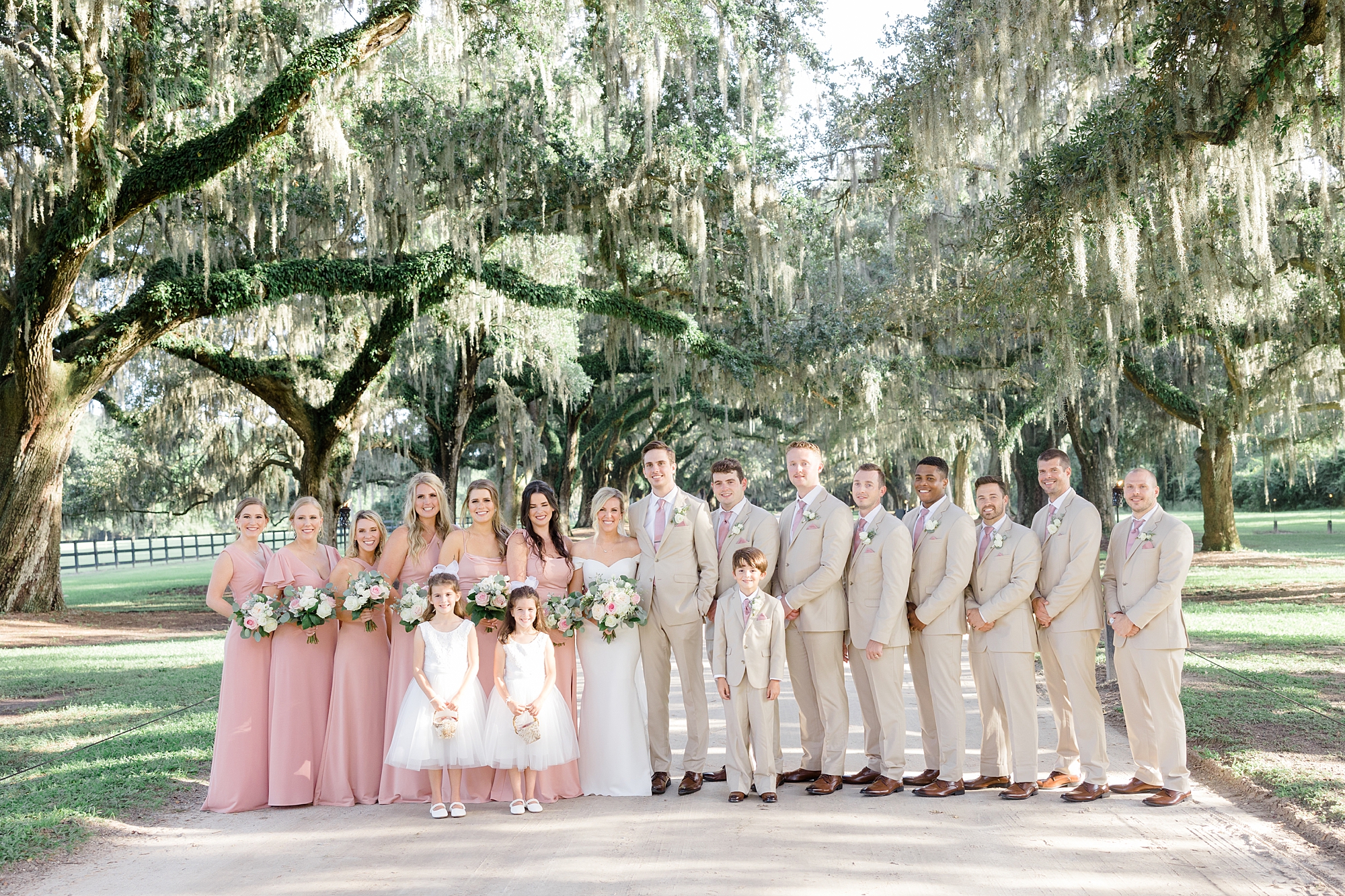 bride and groom stand with wedding party in tan and pink attire