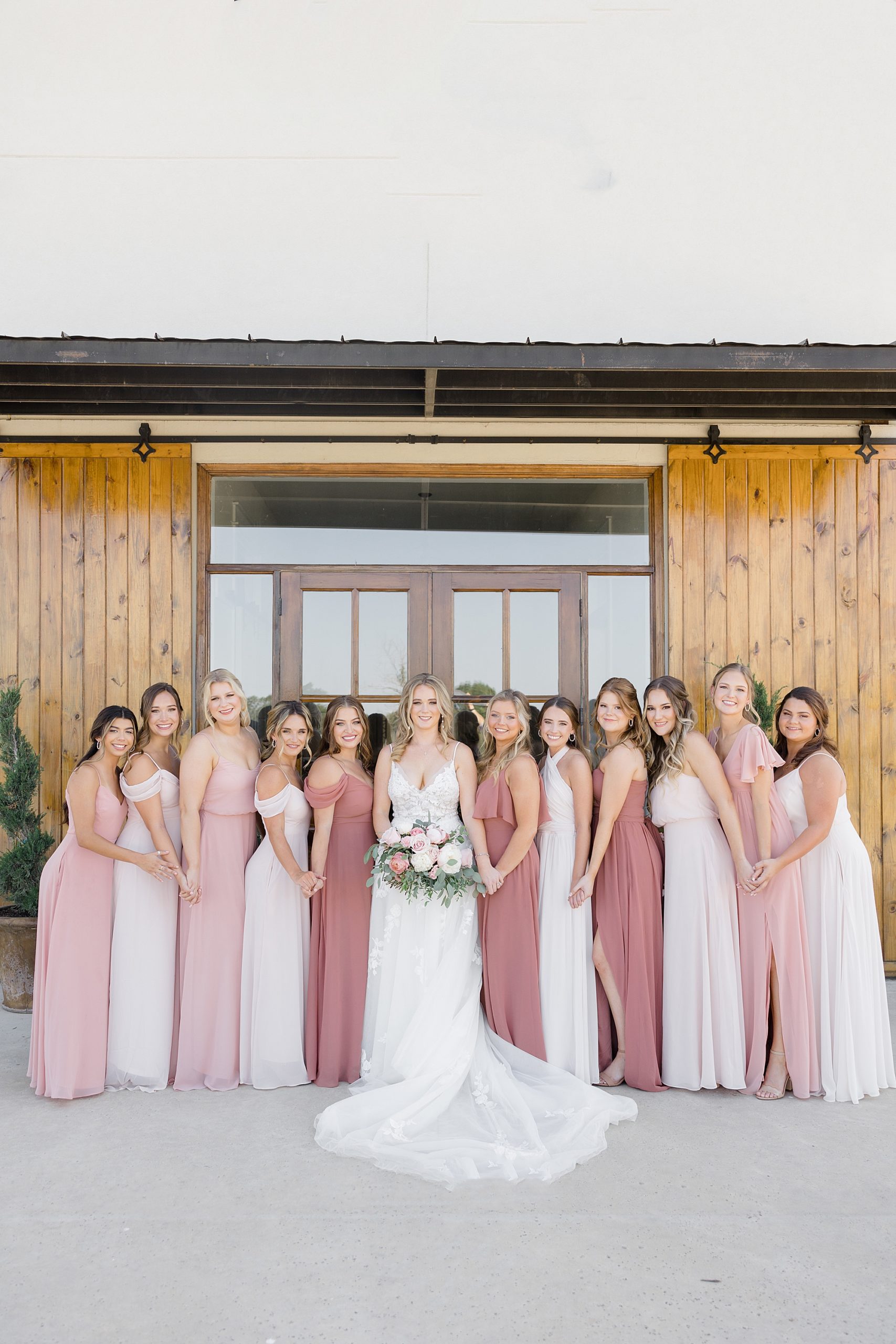 bride and bridesmaids in pink gowns pose outside Oak + Ivy