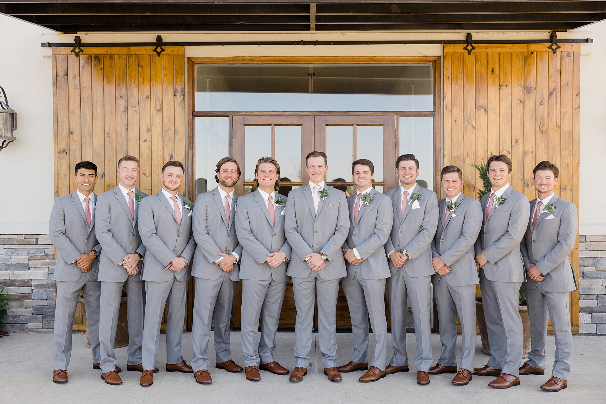 groom and groomsmen in grey suits pose by wooden doors
