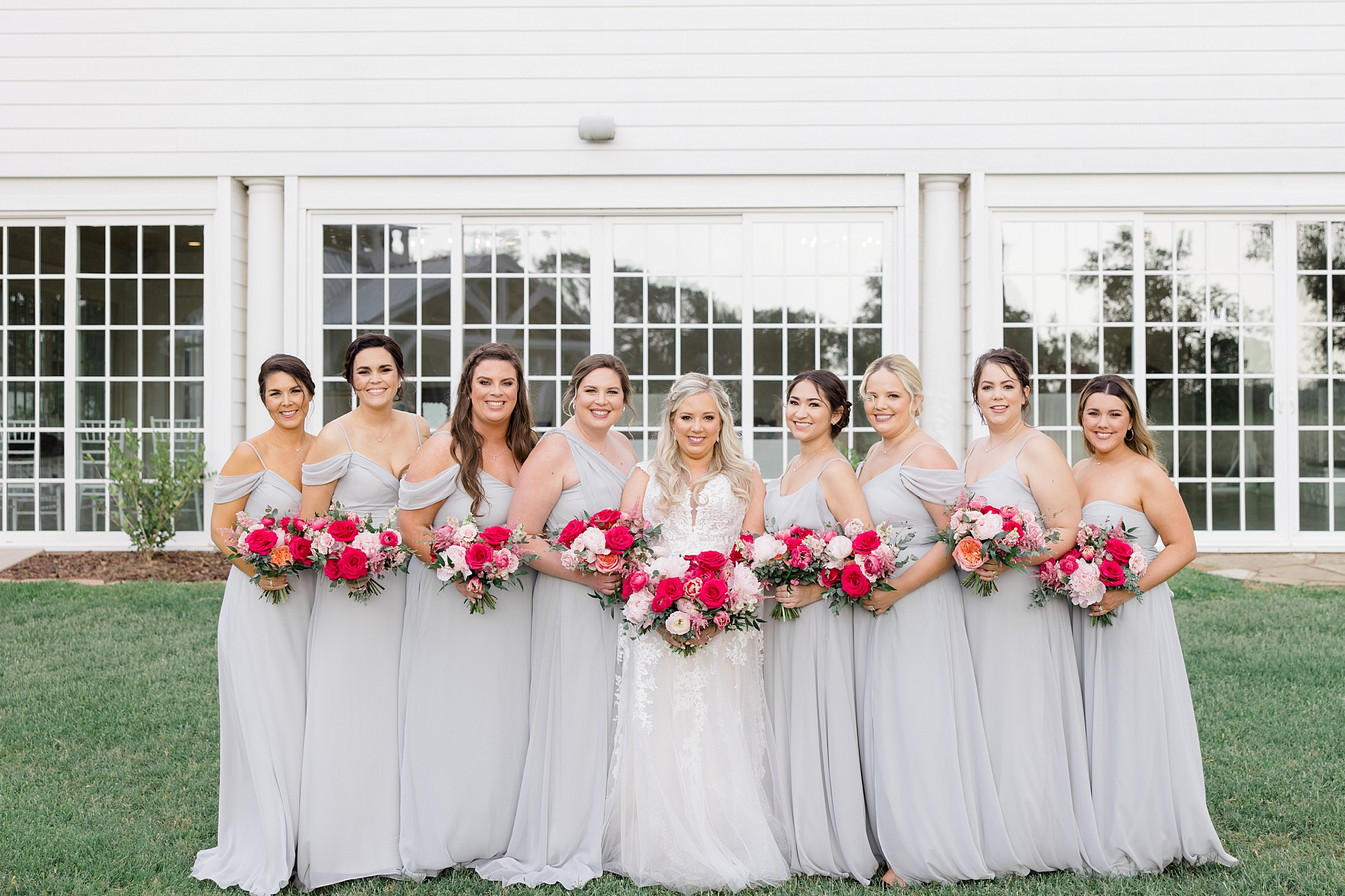 bride stands with bridesmaids holding bright pink bouquets 