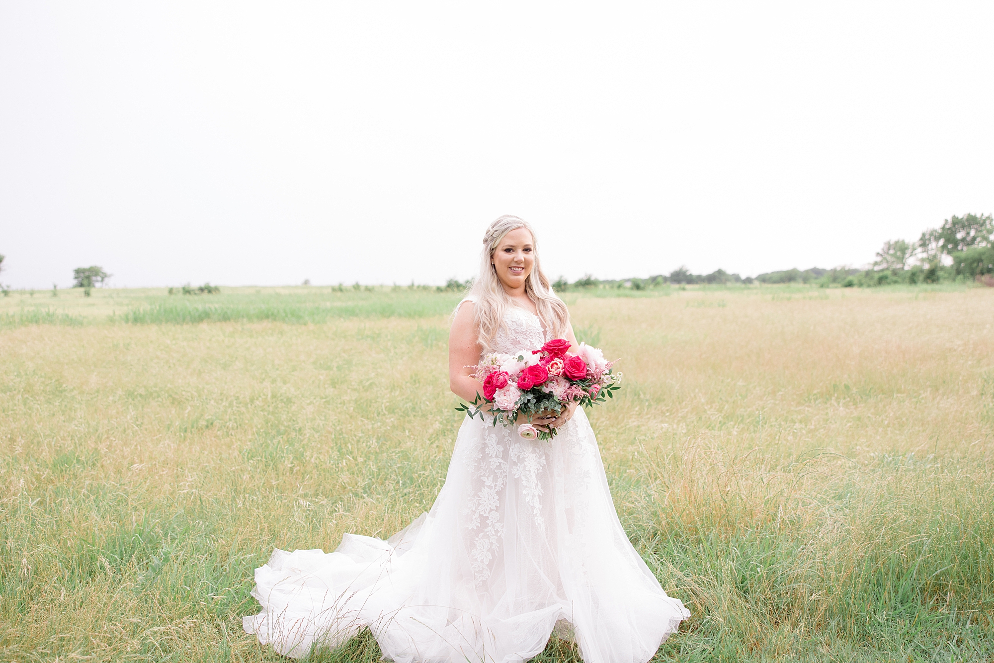 bride poses in field at Willow Creek with bright pink bouquet 