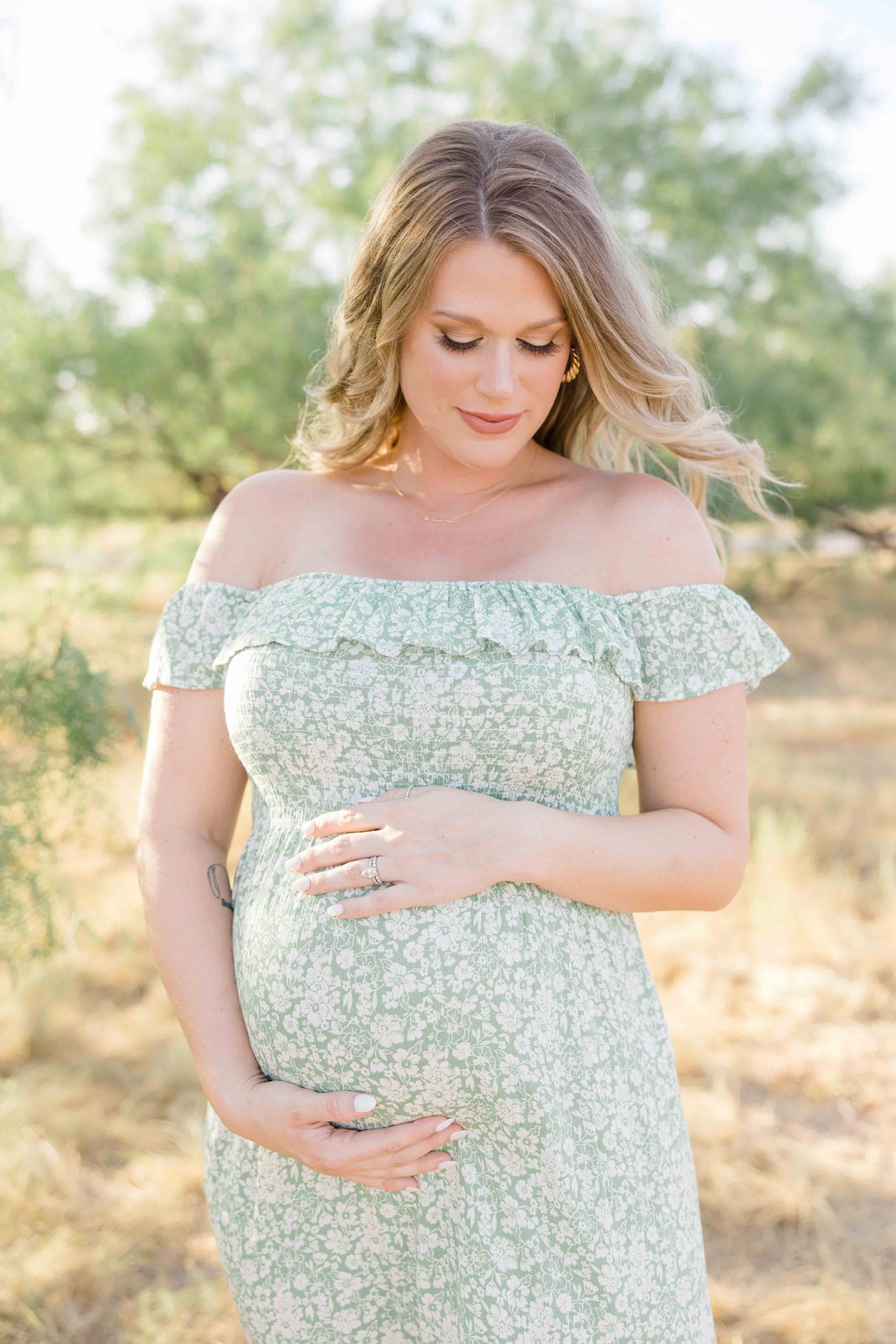 woman stands holding belly in green dress during summer maternity photos