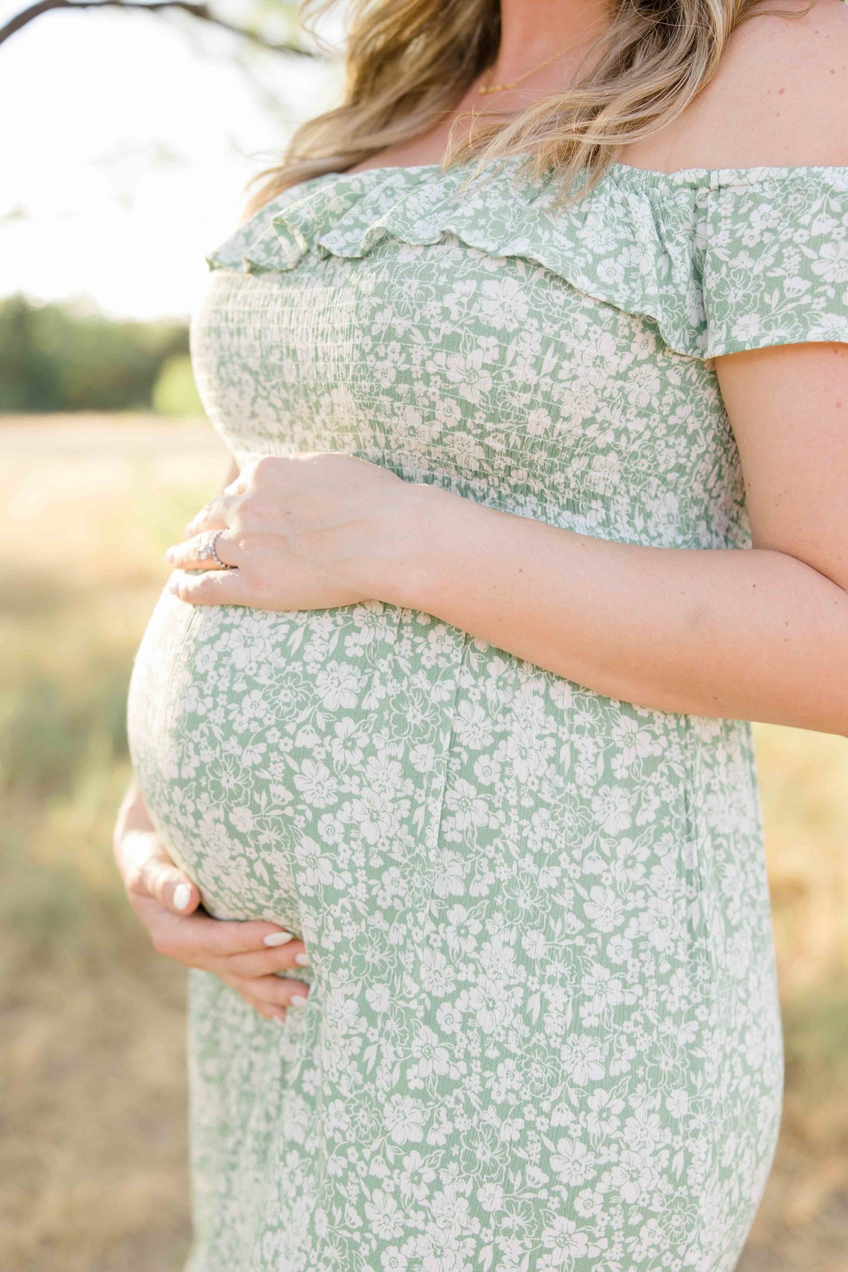 woman holds belly in green dress during summer Murrell Park maternity session