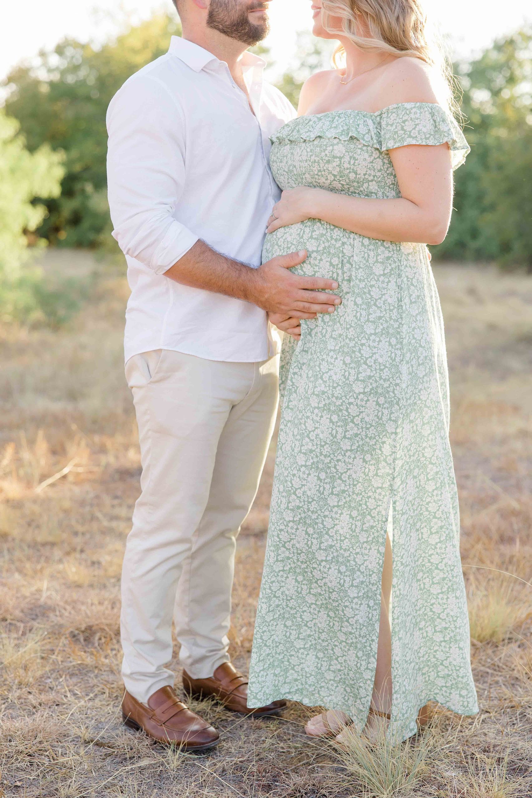woman in green dress holds baby bump during maternity photos