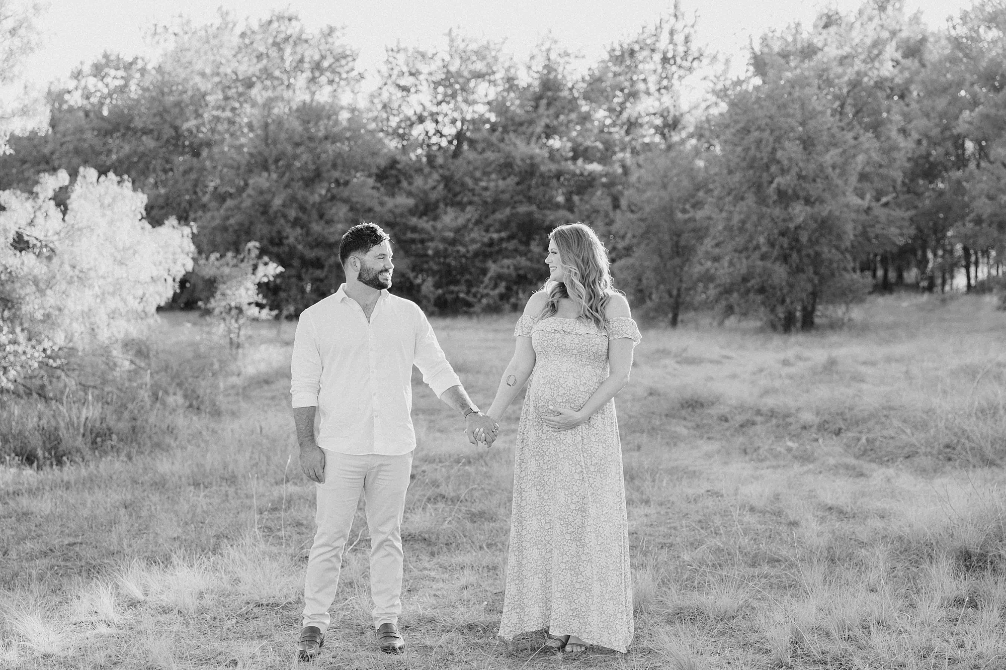 husband and wife hold hands in field during Murrell Park maternity session