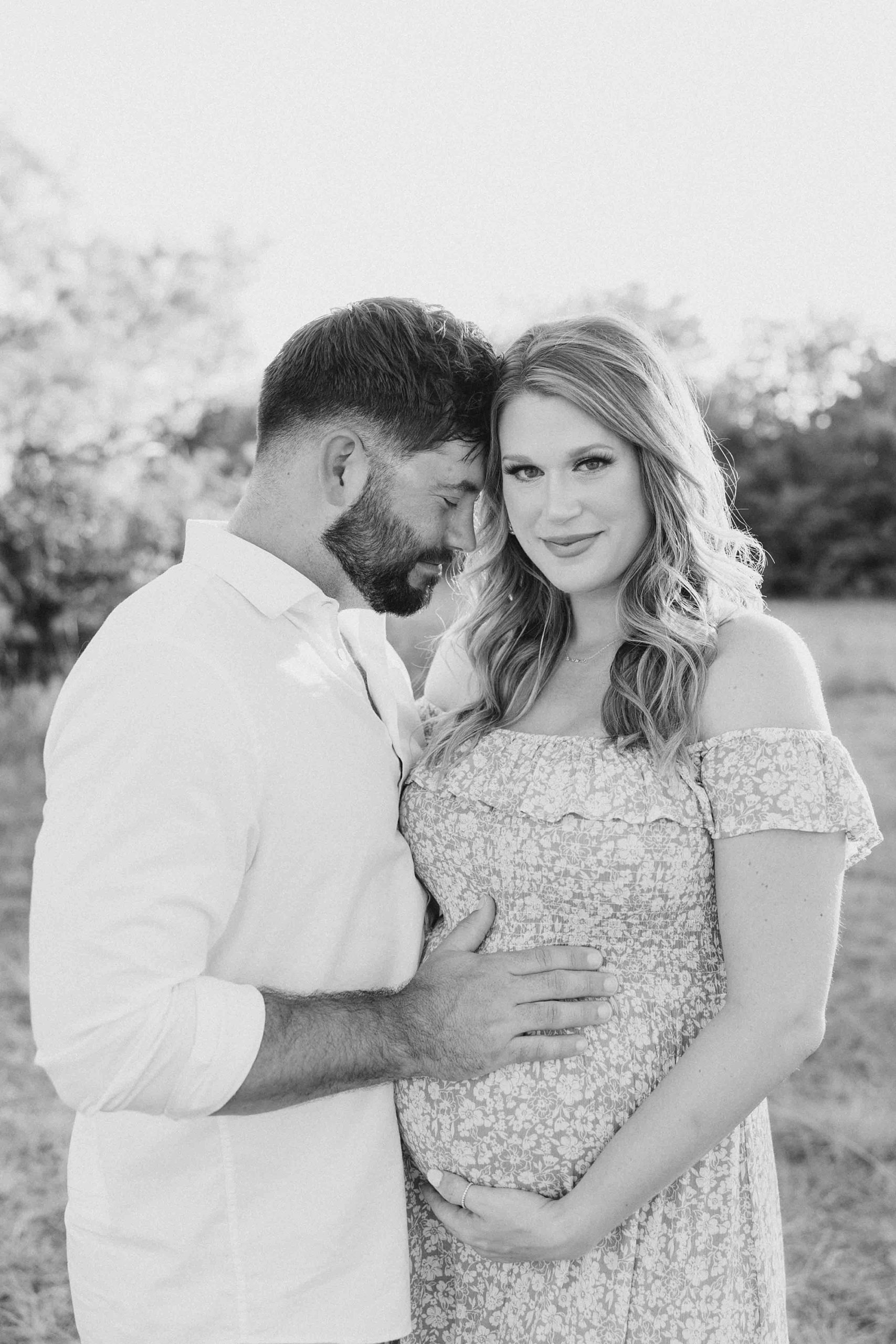 man leans into wife's forehead while holding her baby bump