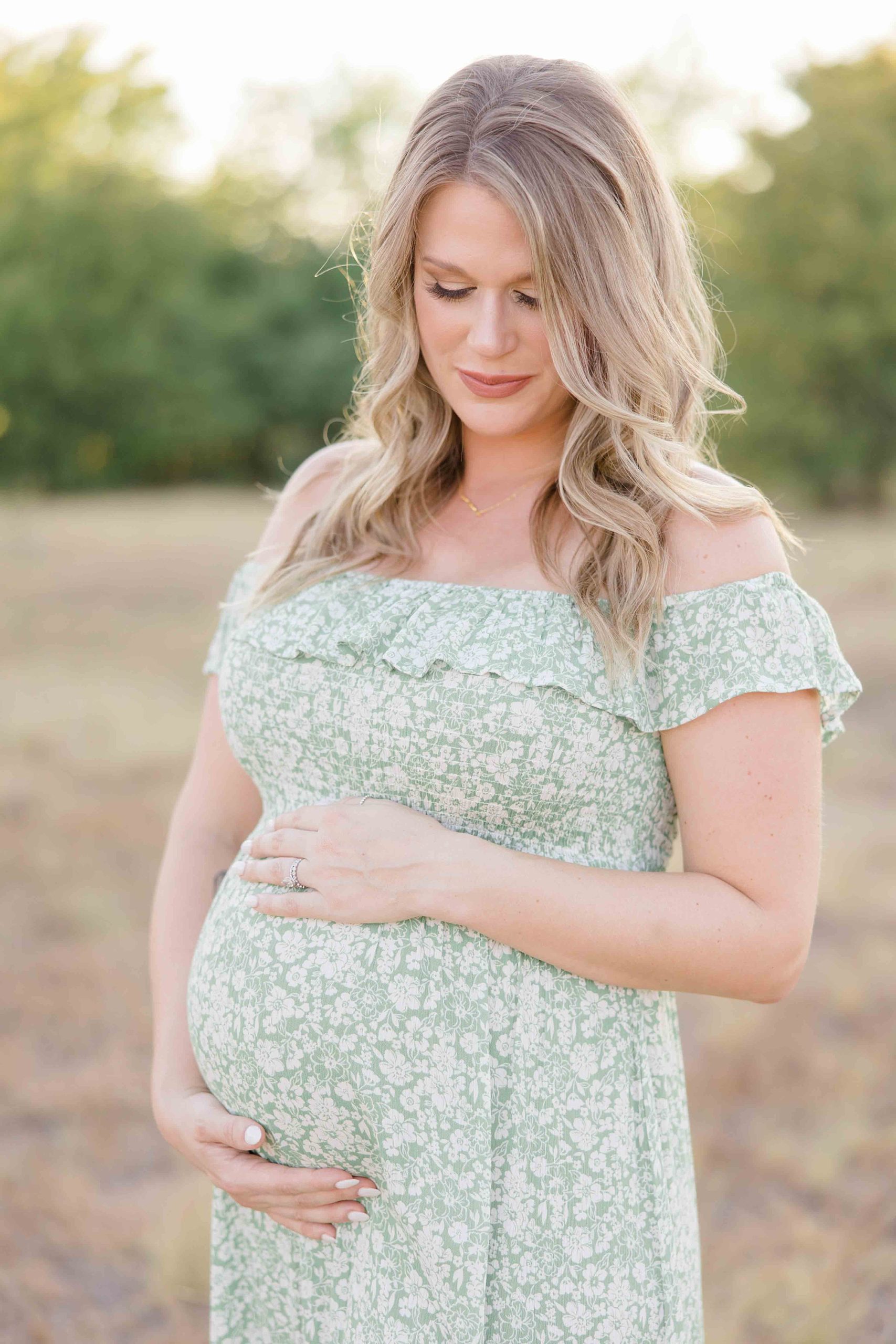mother in green dress holds baby bump during maternity photos