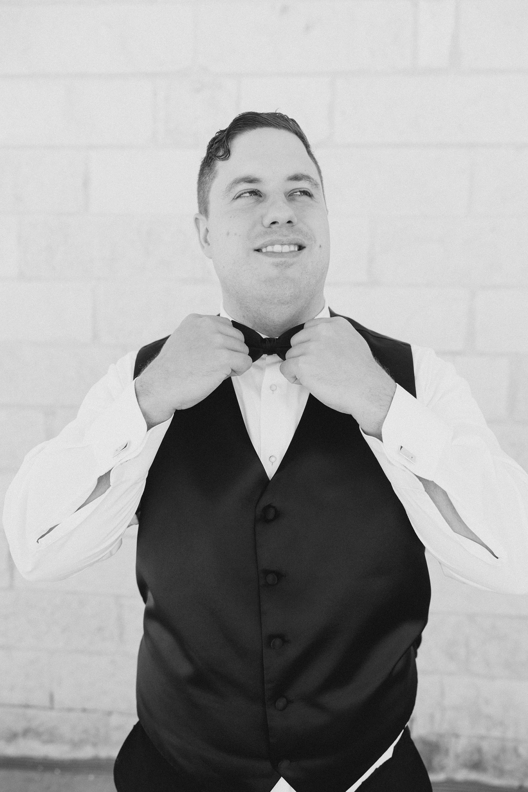 groom adjusts bowtie in black vest 