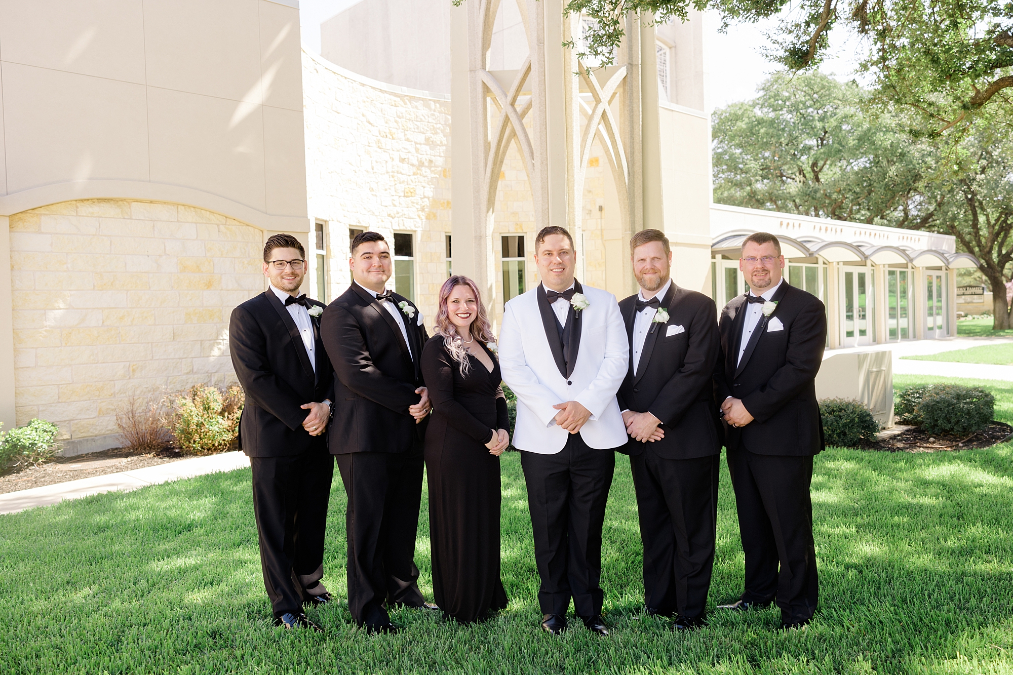 groom stands with groomsmen in classic black suits outside church in Texas 