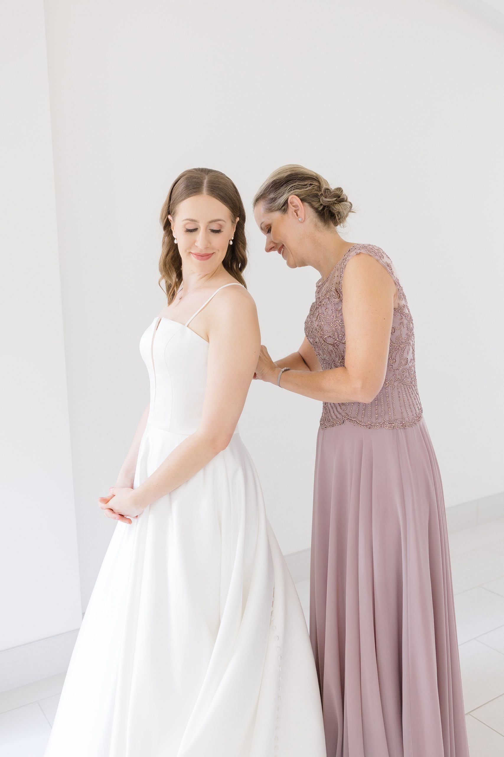 bridesmaid in pink gown helps bride into wedding gown