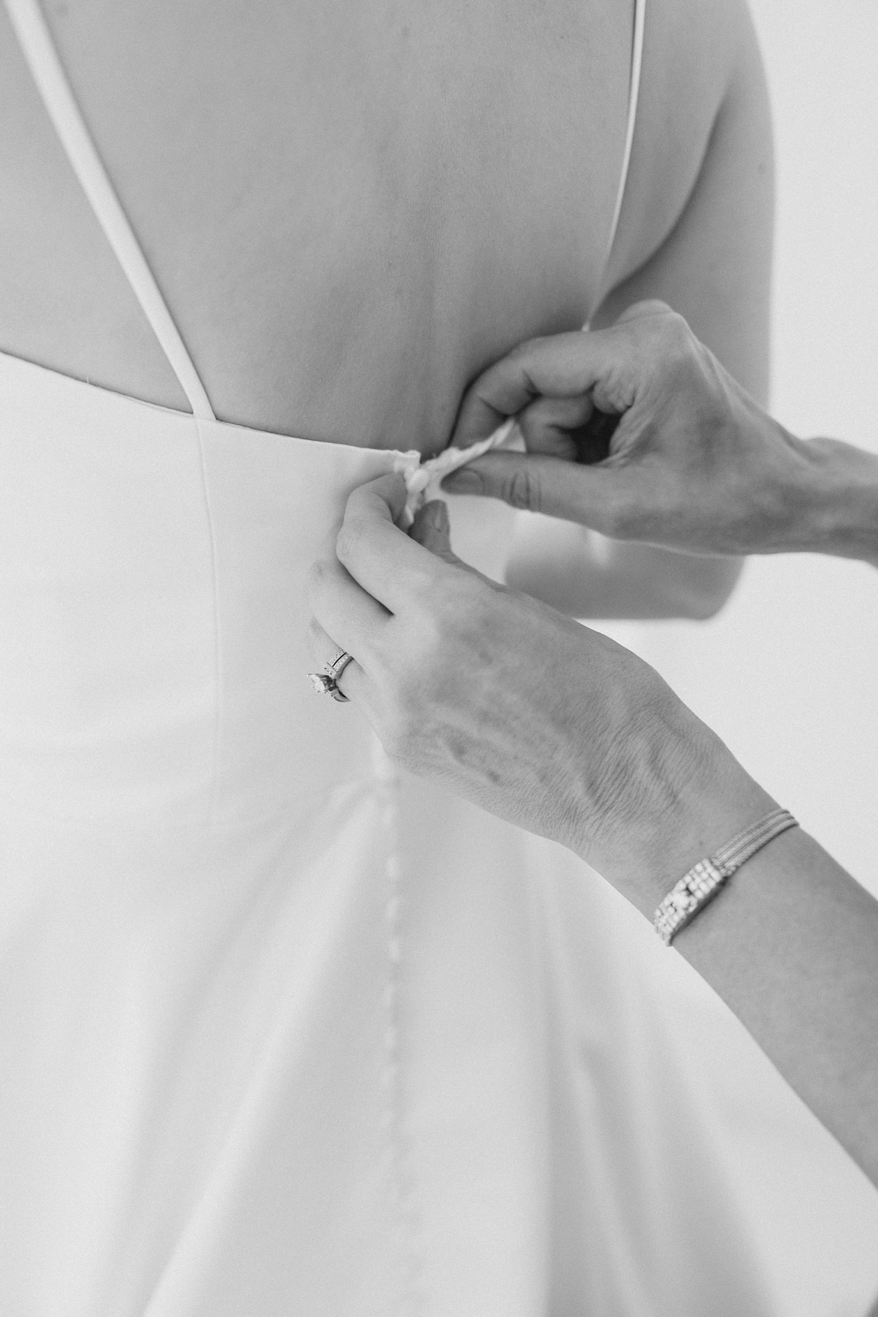 woman helps bride with buttons on wedding gown 