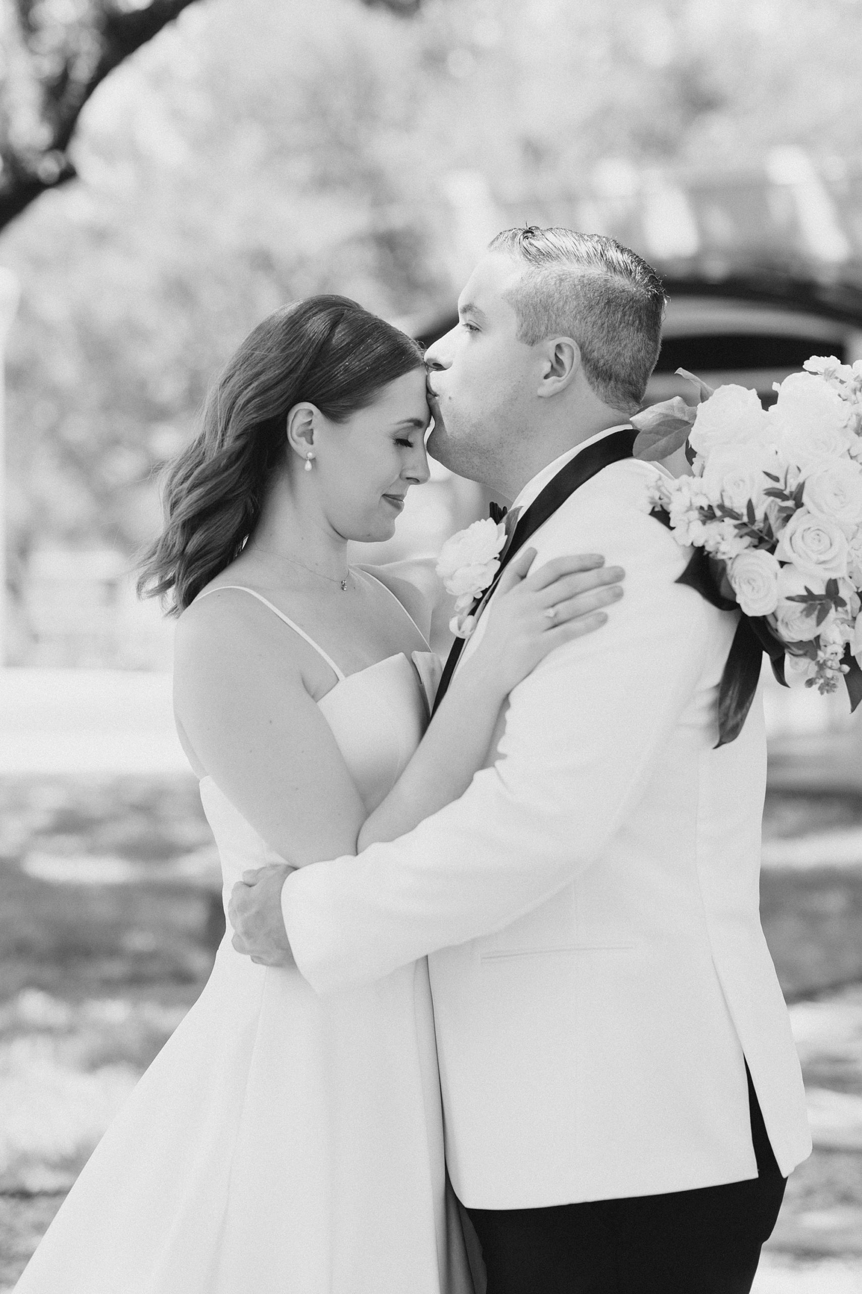 groom kisses bride's forehead during portraits under trees in Fort Worth TX