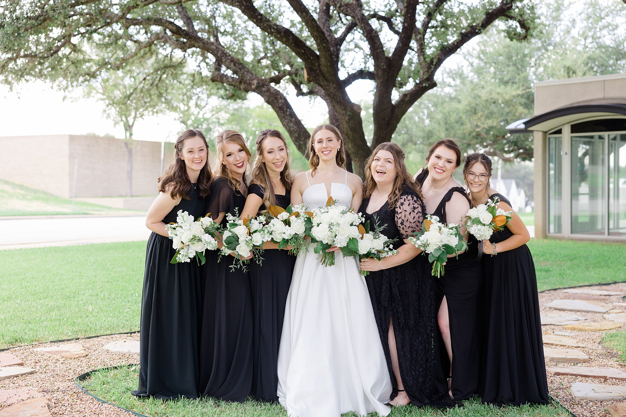 bride stands with bridesmaids in mismatched gowns with ivory white bouquets 