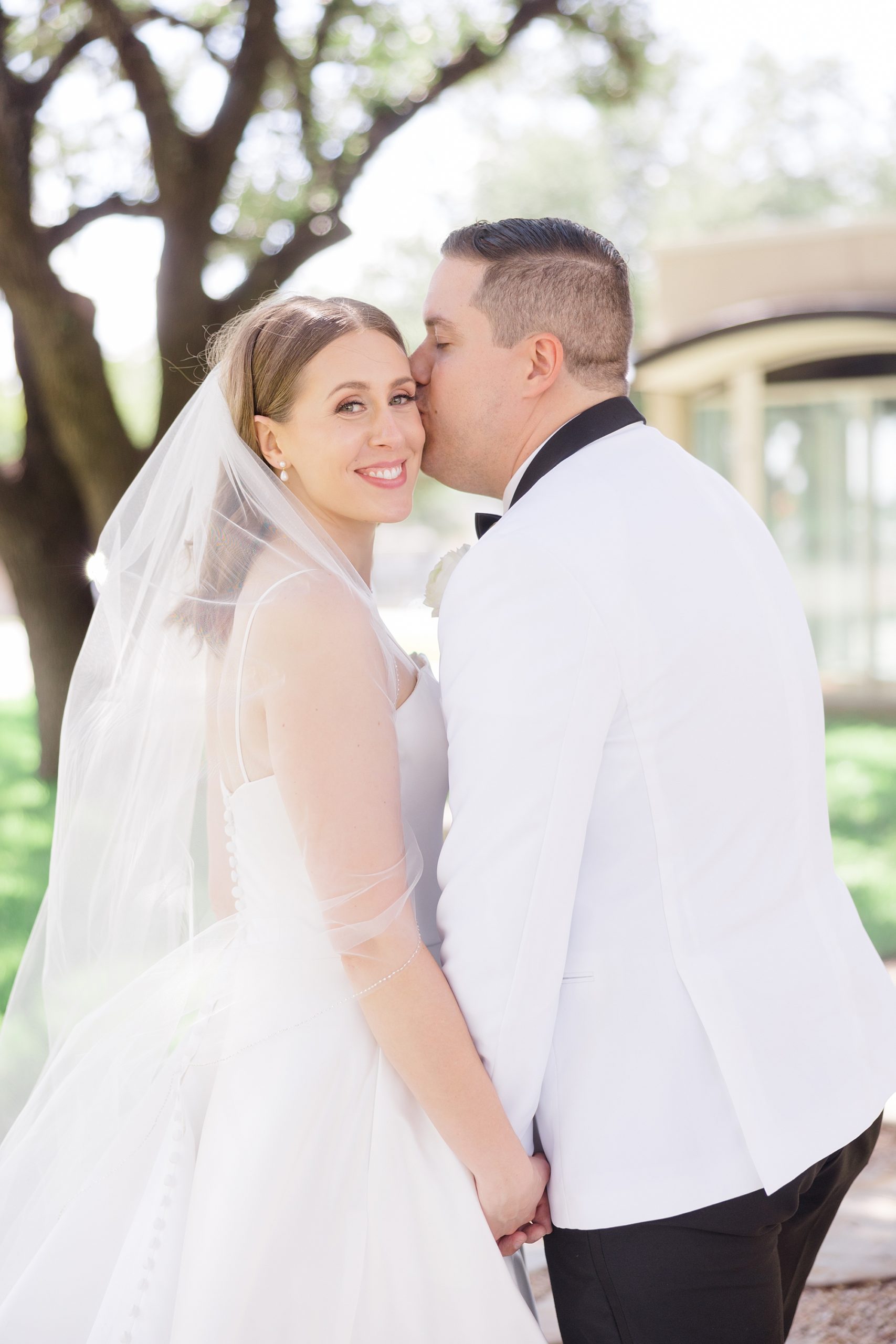 groom kisses bride's forehead during portraits outside Holy Family Catholic Church
