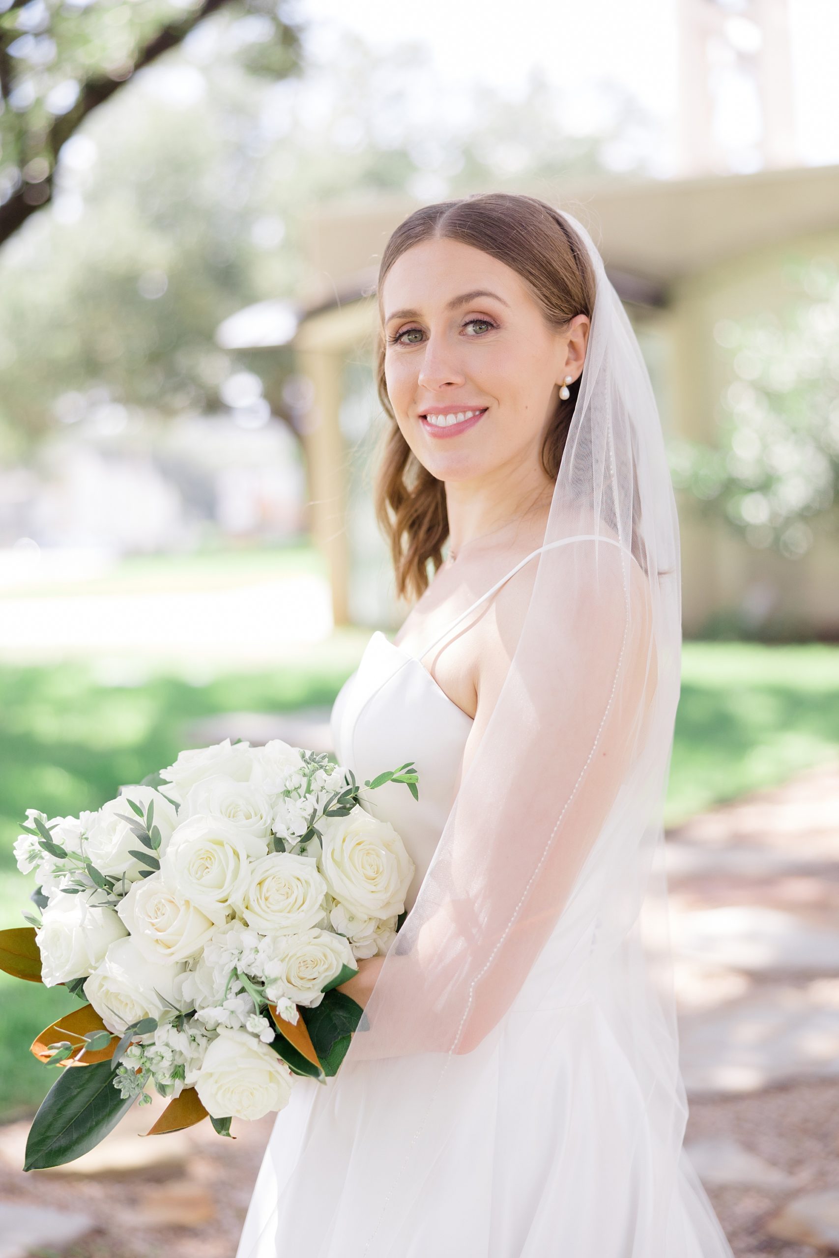 bride smiles with veil around arm holding bouquet of ivory roses 