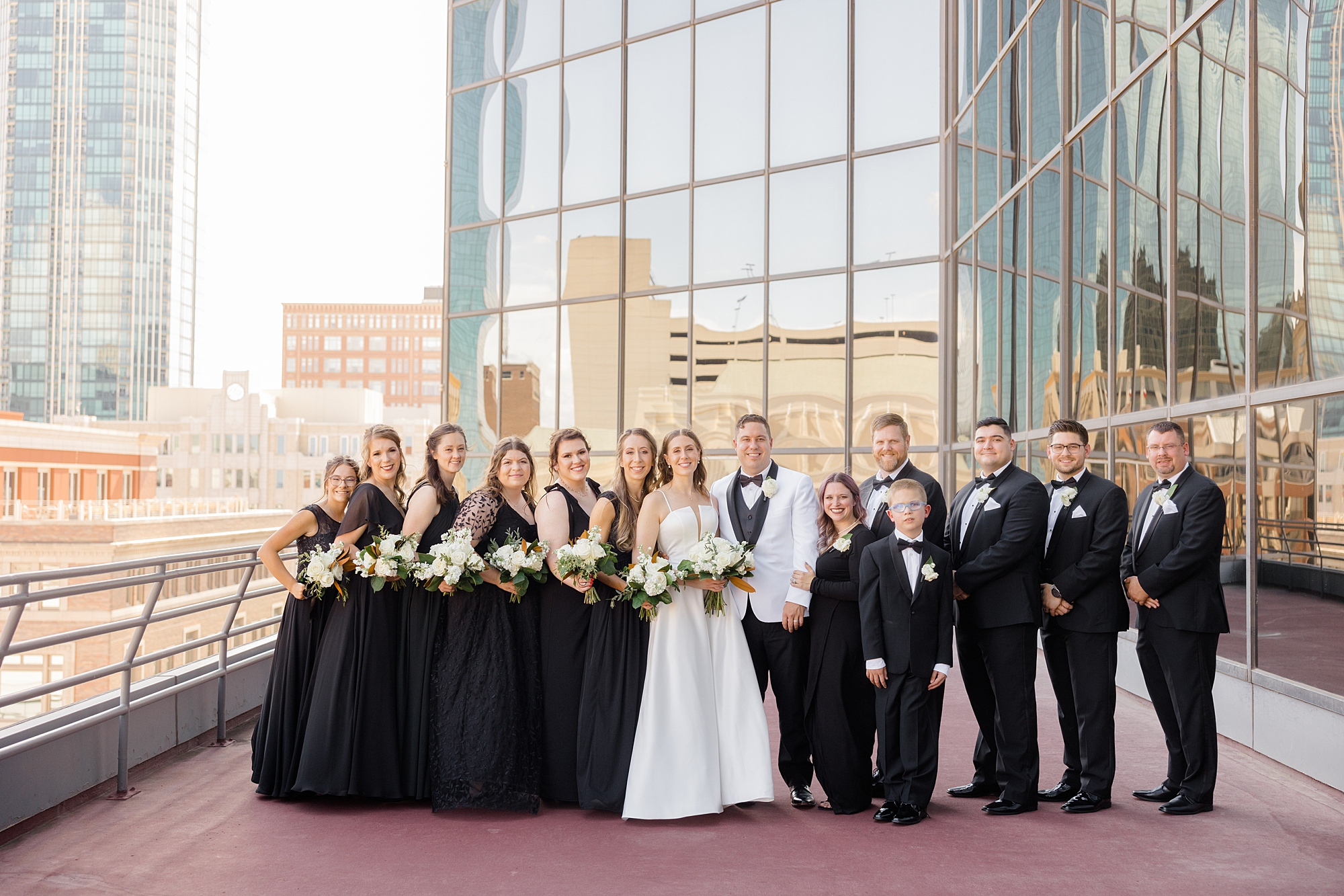 bride and groom stand with wedding party in black attire outside the Fort Worth City Club