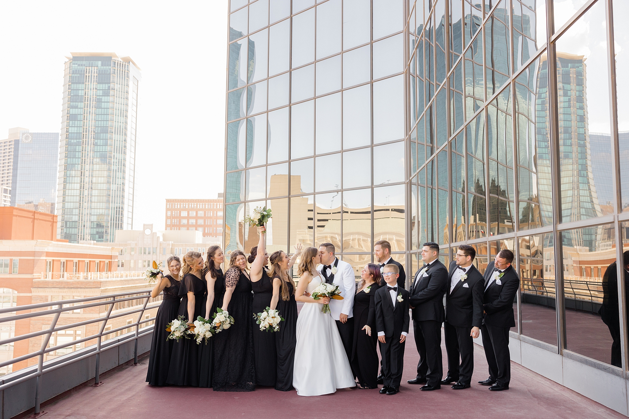 newlyweds kiss with wedding party around them on the balcony of Fort Worth City Club