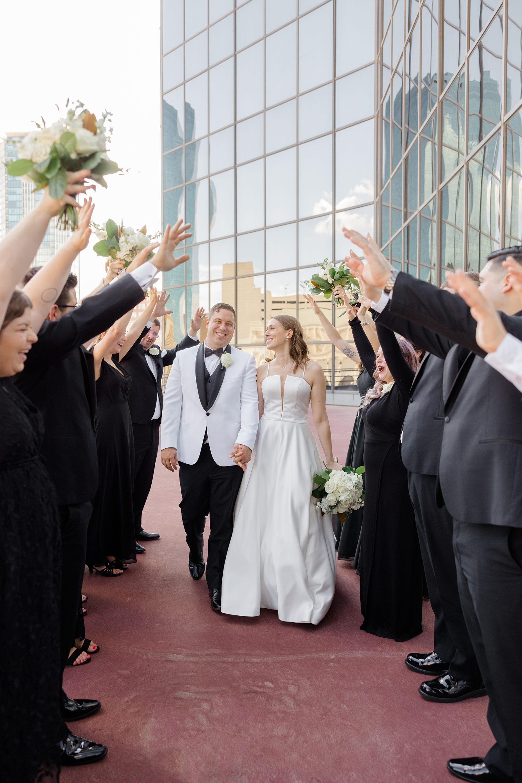bride and groom hold hands smiling walking under arms of bridal party 