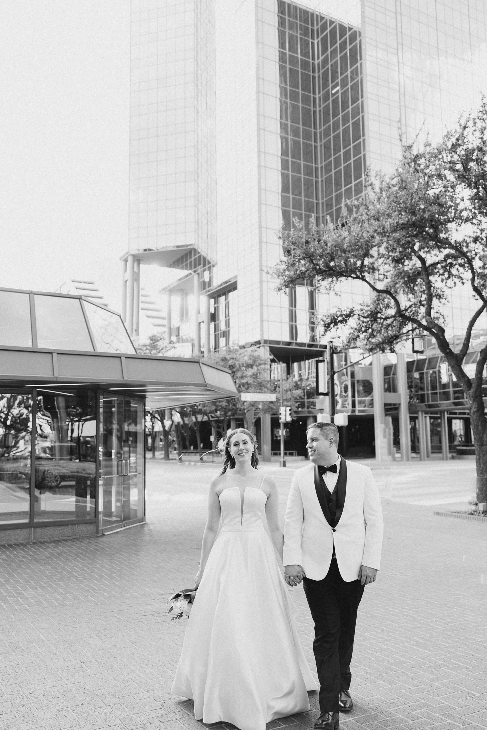 bride and groom hold hands walking outside Fort Worth City Club