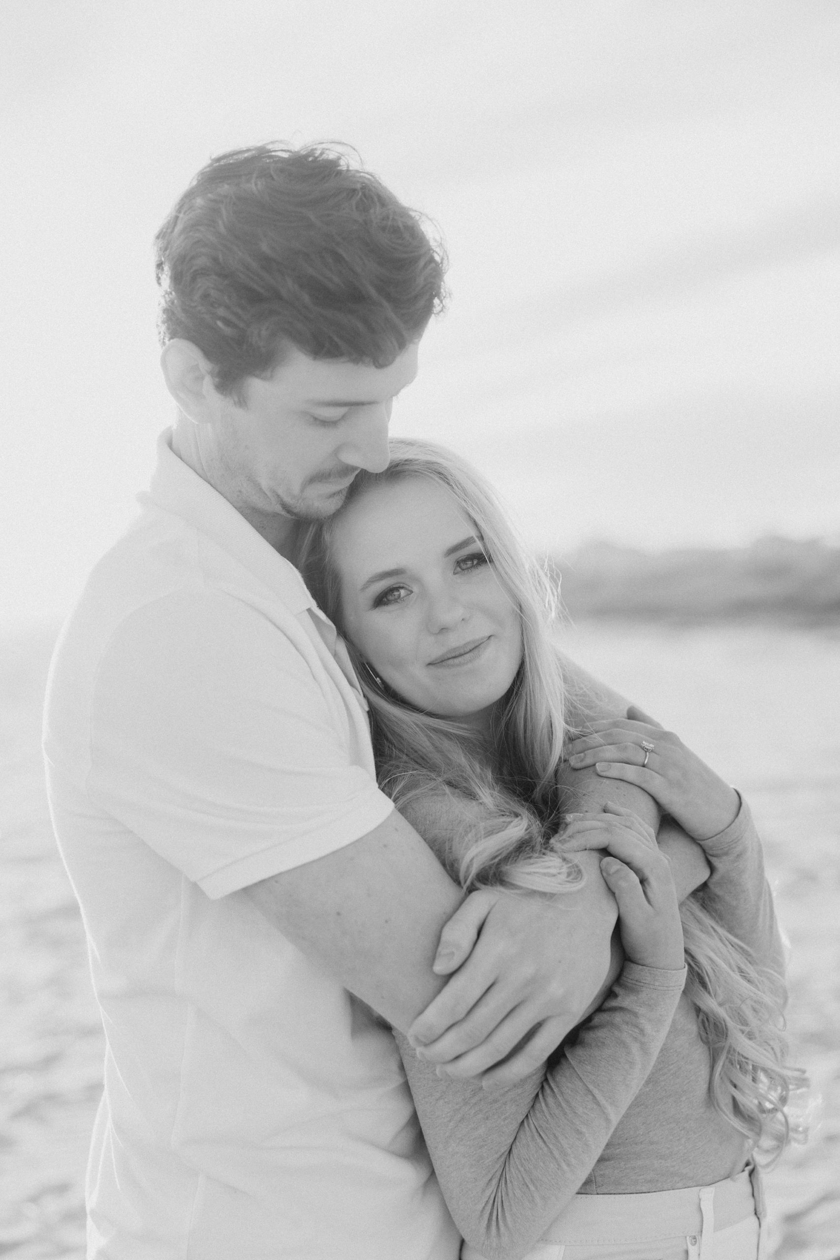 man hugs woman against his chest during winter beach engagement session