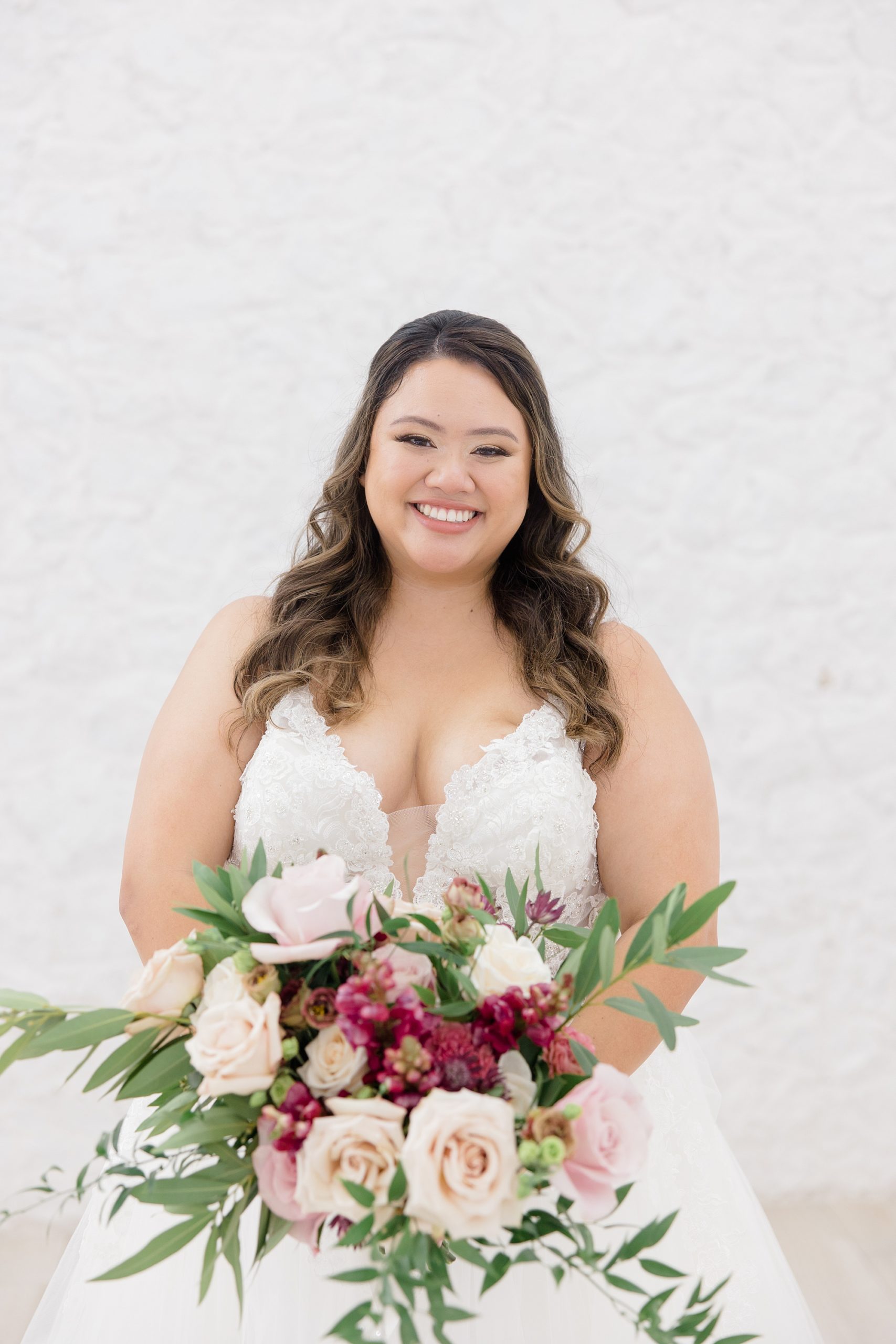 bride stands holding bouquet of pink flowers in front of gown 