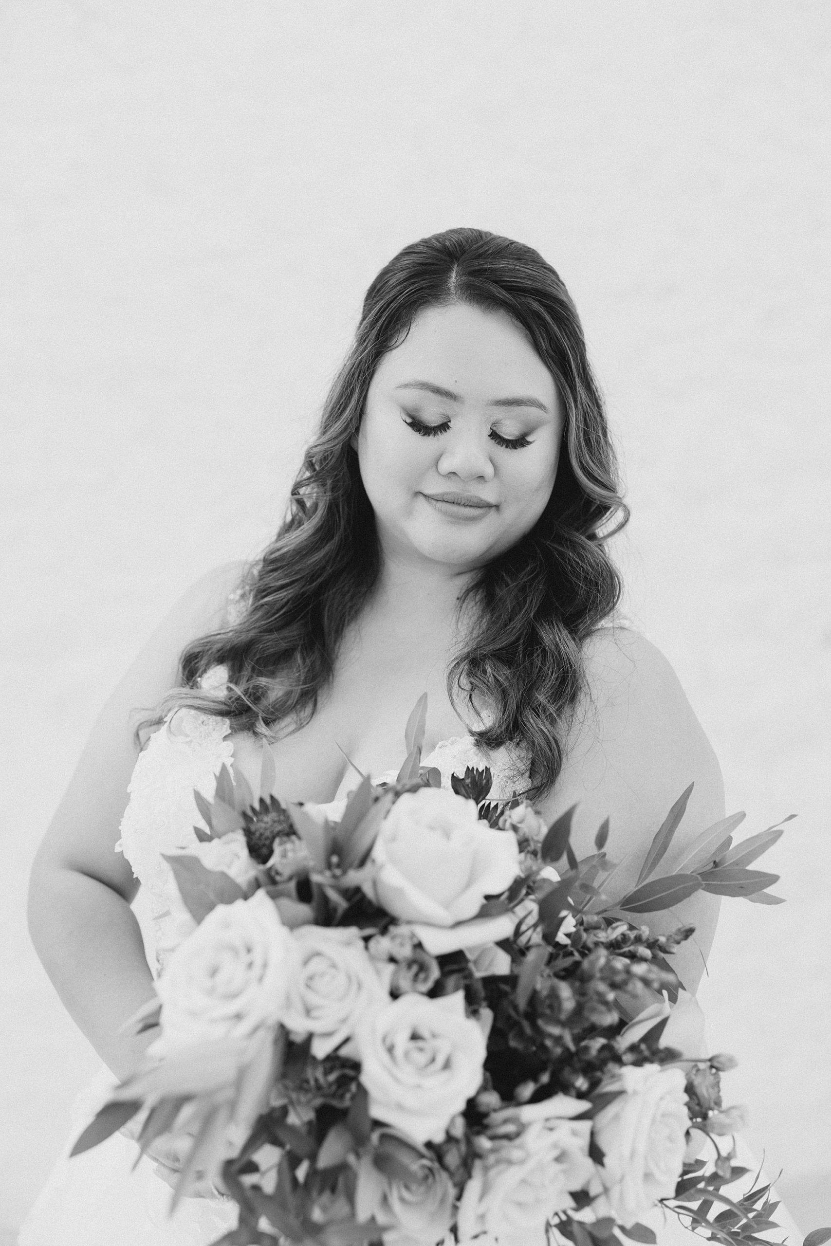 black and white portrait of bride looking down at bouquet 