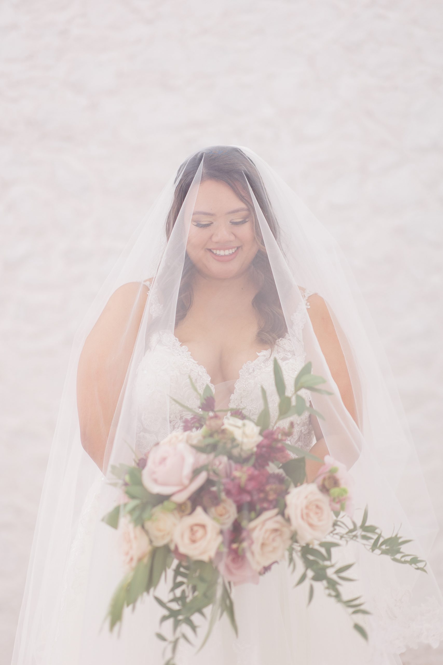 bride holds bouquet of pink flowers under veil at The Nest at Ruth Farms