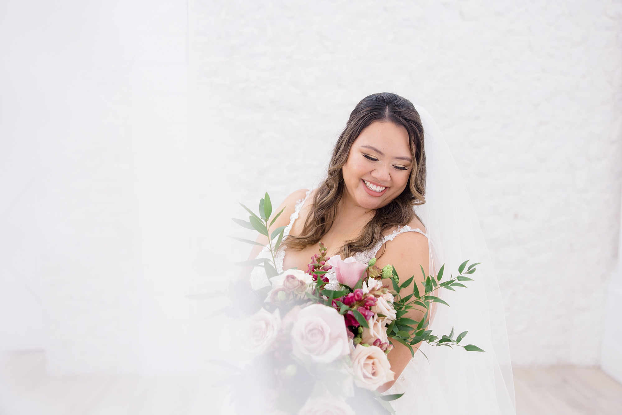 bride smiles over shoulder down at bouquet of pink flowers 