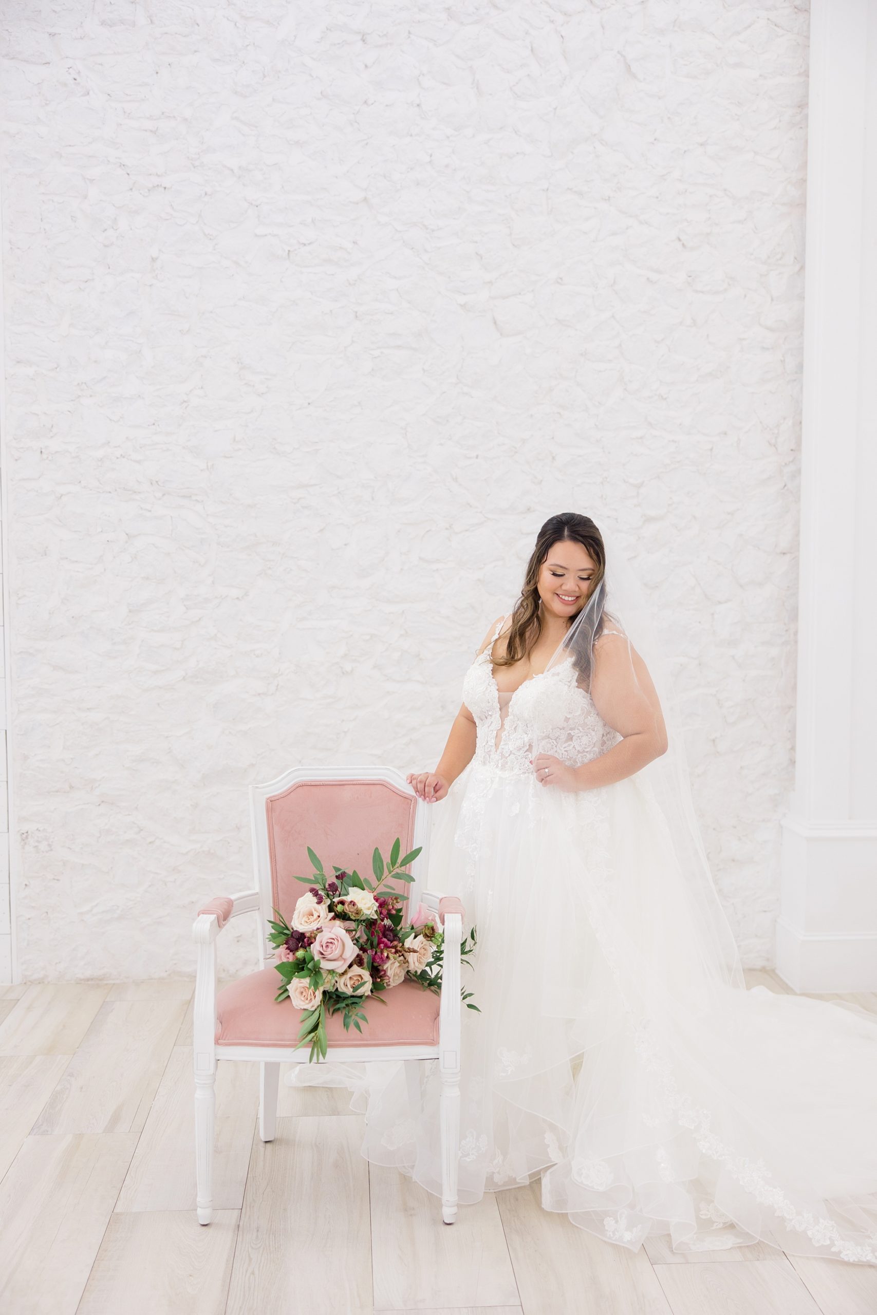 bride holds top of pink ad white chair by white brick wall at The Nest at Ruth Farms